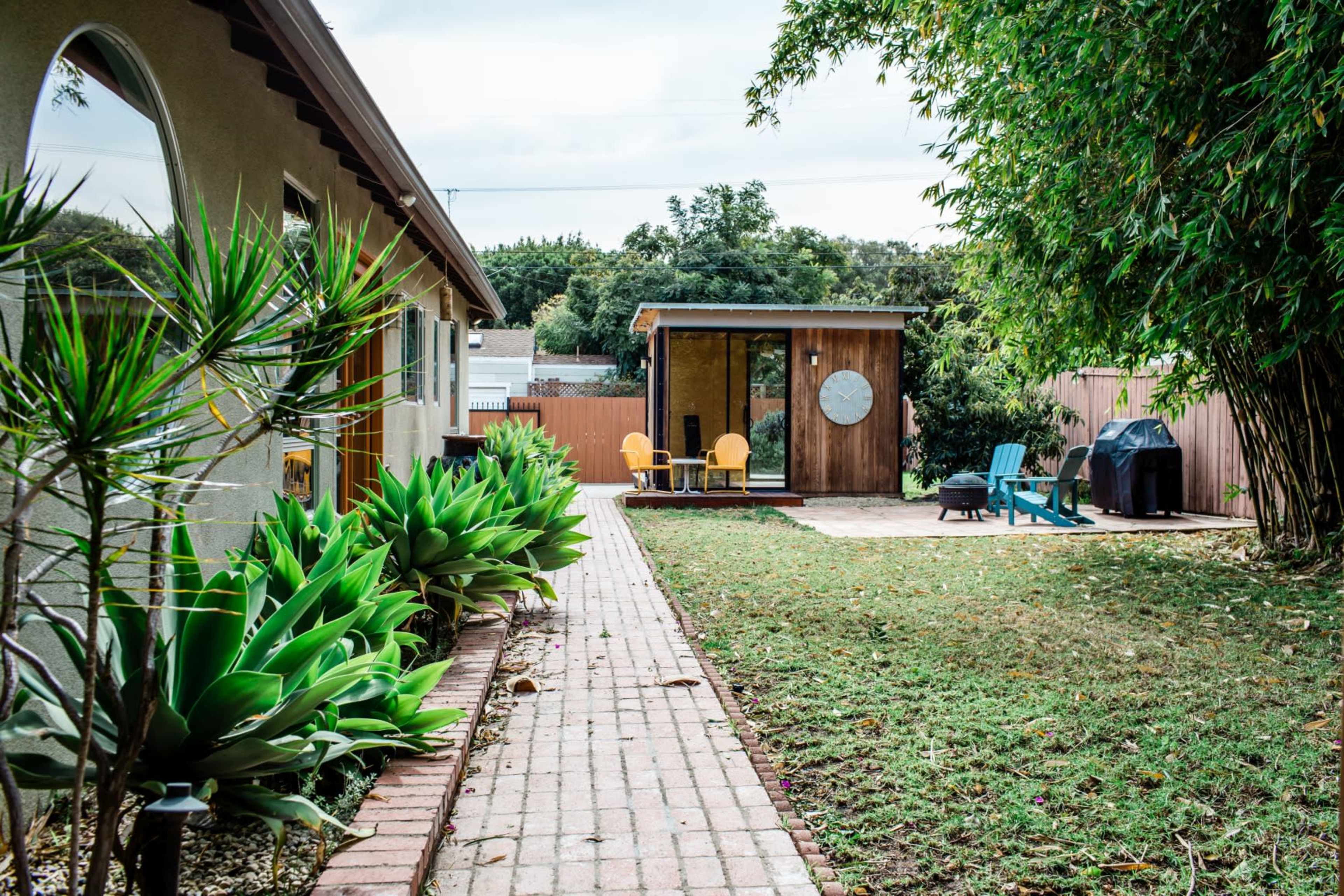 A series of brick pathways lead through a garden area with succulents, flanked by a modern shed and a small patio with chairs.