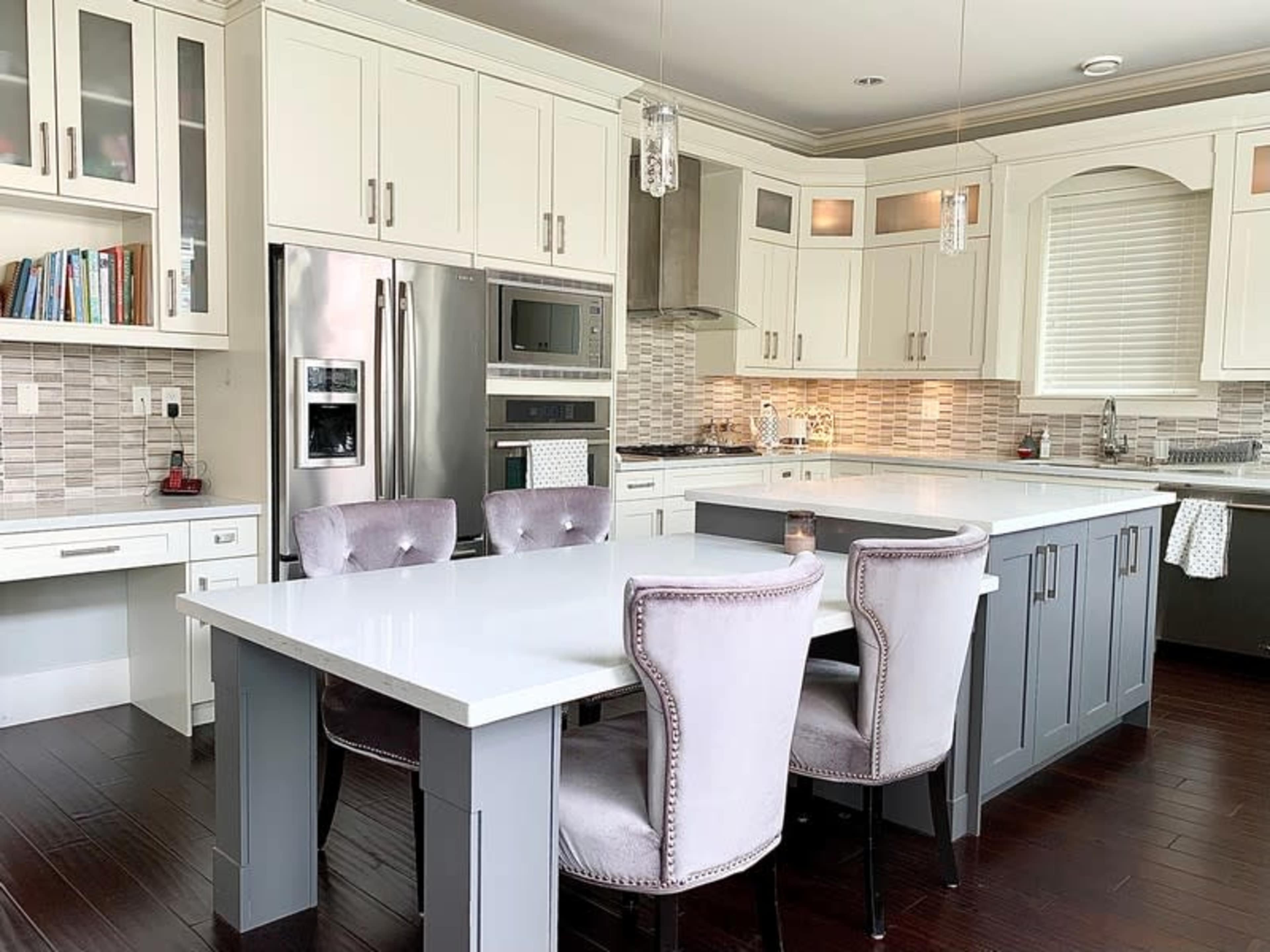 A modern kitchen featuring white cabinetry, stainless steel appliances, and a central island with gray accents and upholstered chairs.