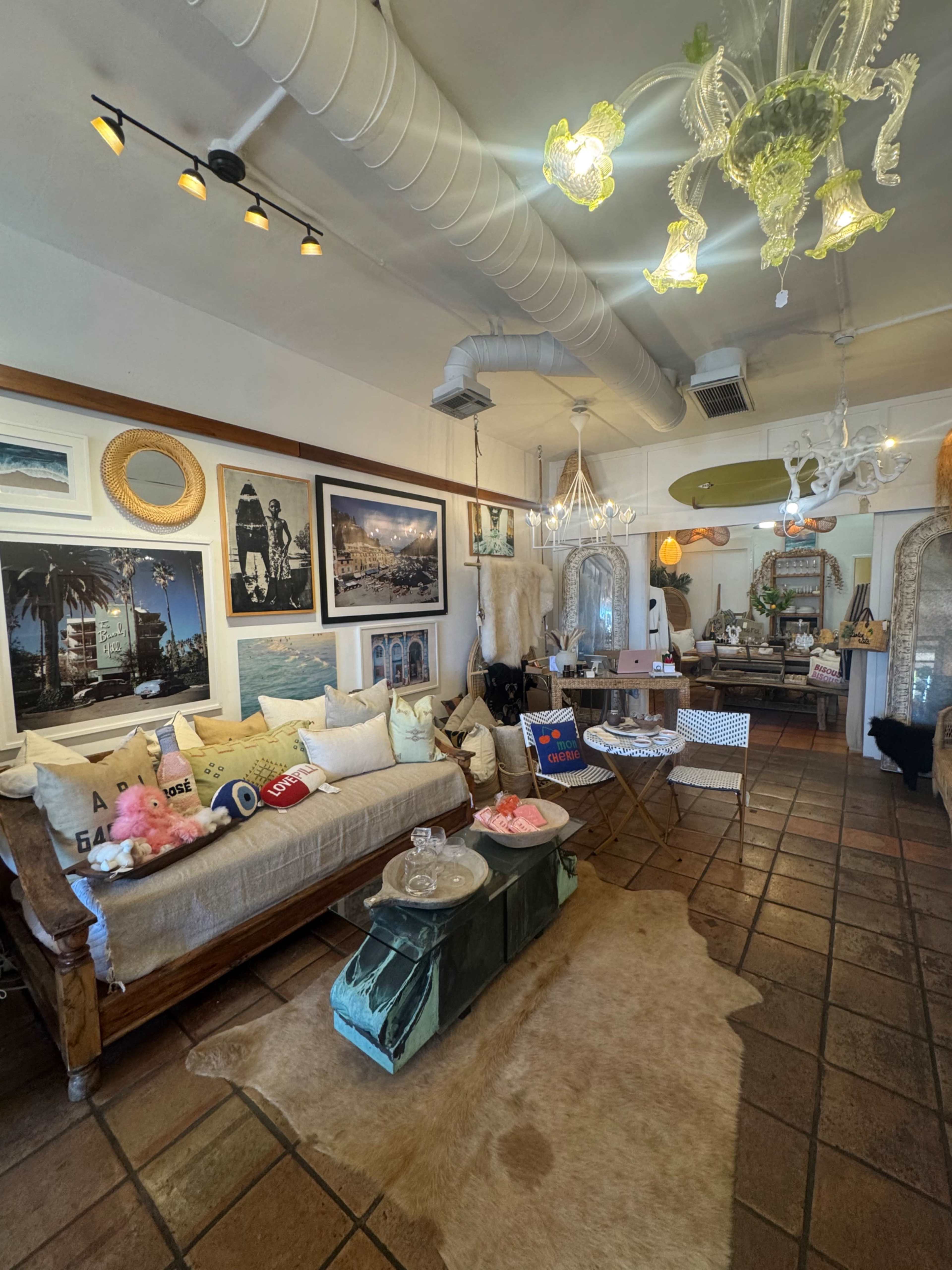 The image shows a stylish boutique with a plush sofa adorned with decorative pillows, framed artwork on the walls, and various decorative items scattered throughout the space.