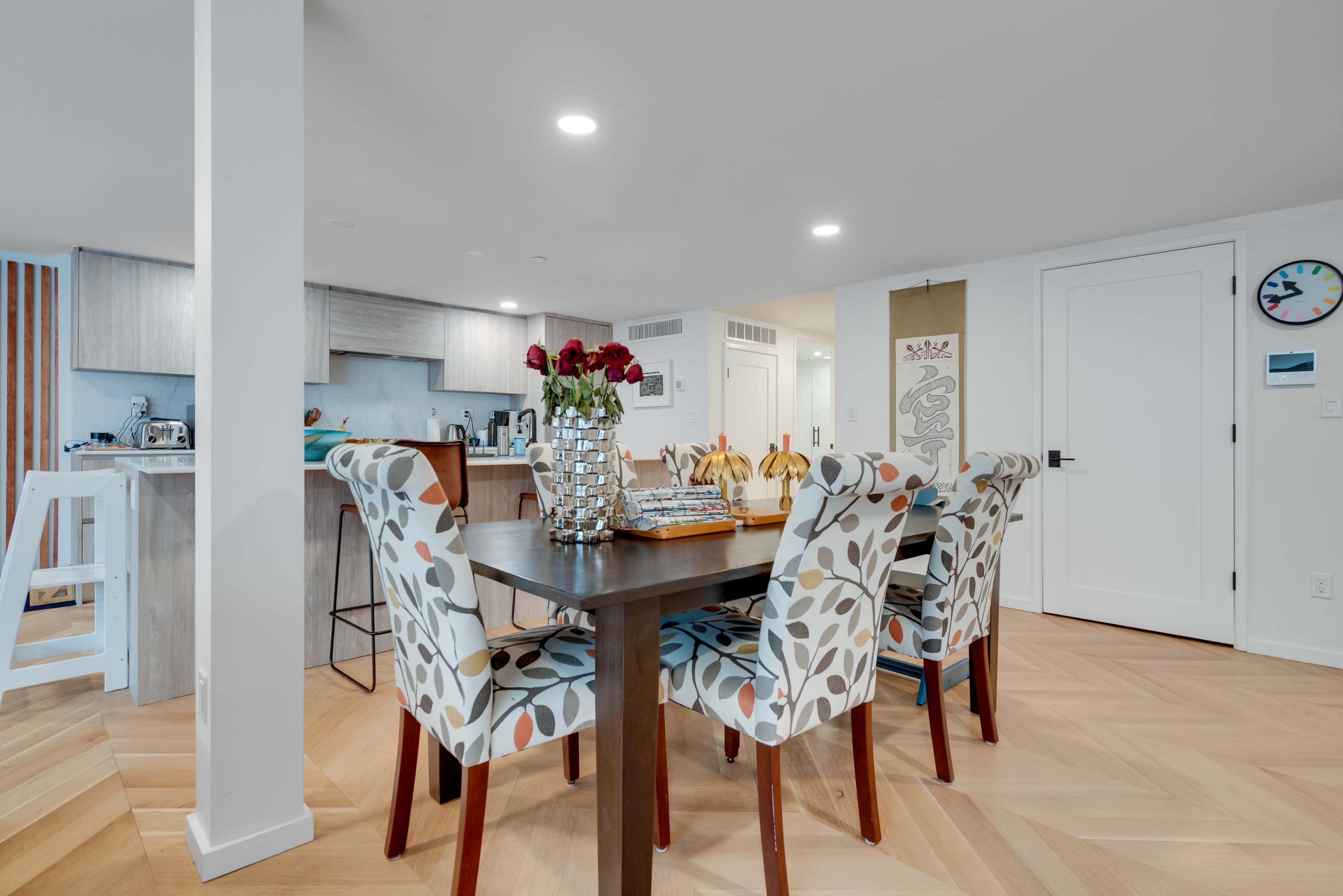 A dining area features a table surrounded by four patterned chairs with a vase of roses on top.