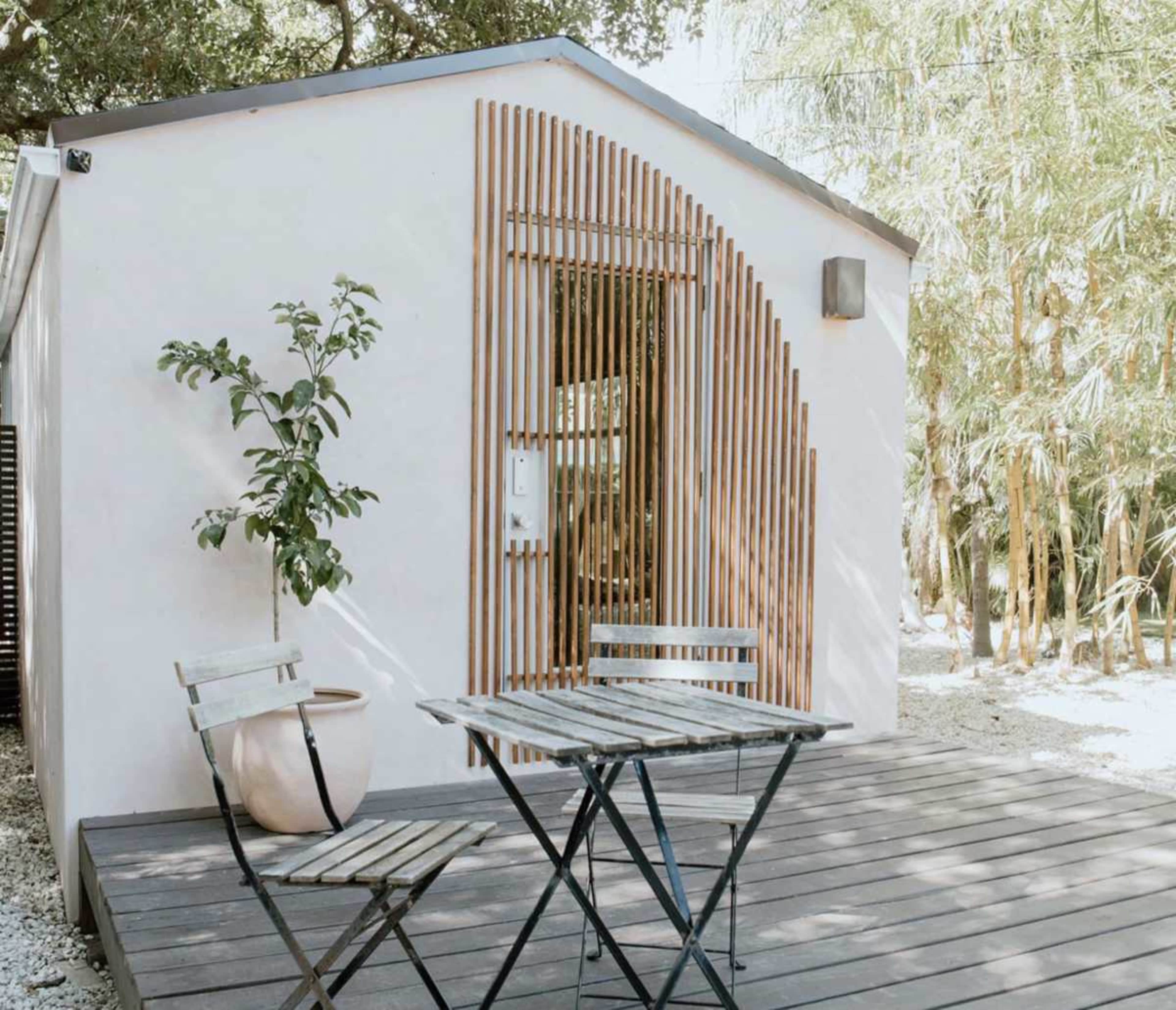 A small, modern white building features wooden slat designs on the door and a patio area with a metal table and chairs.