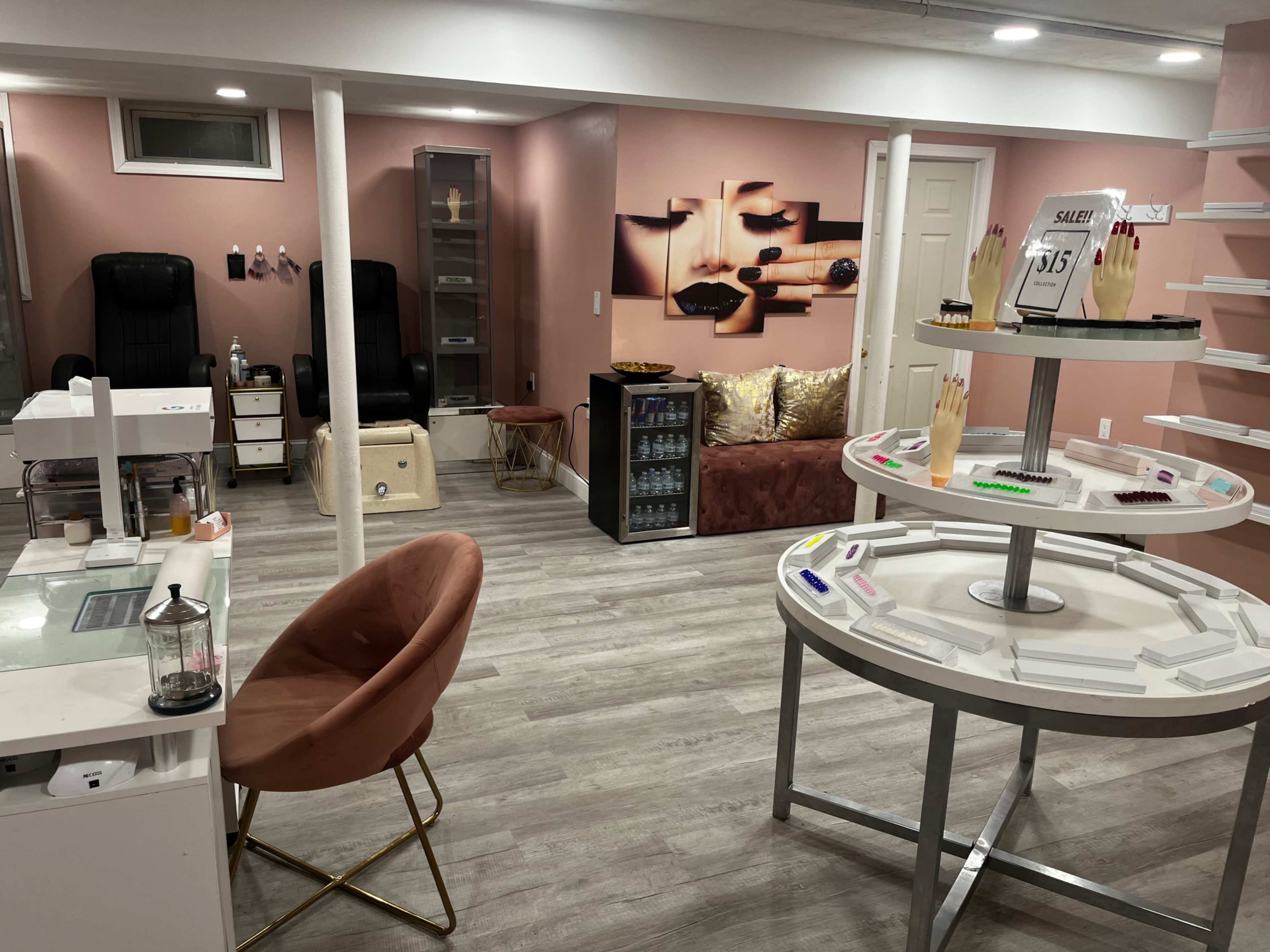 A modern salon interior with nail stations, a seating area, and a display table featuring nail products.