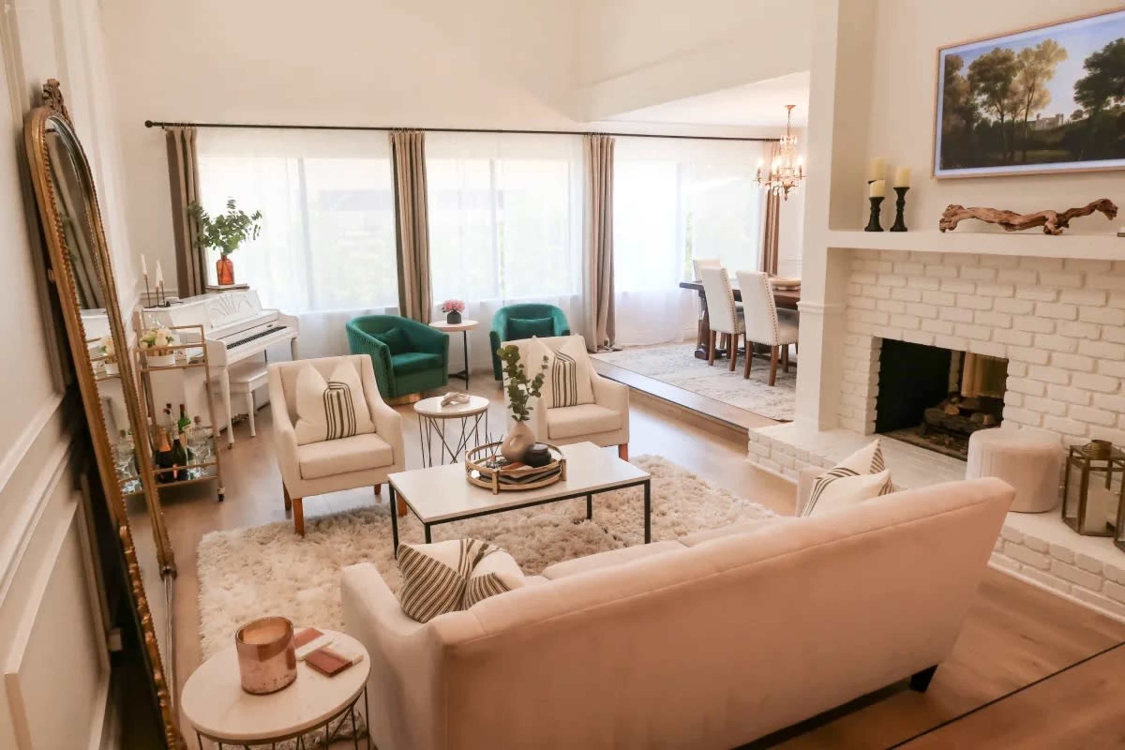 The scene depicts a bright, modern living room featuring a plush white sofa, green chairs, a coffee table, and a fireplace with a light-colored brick surround.