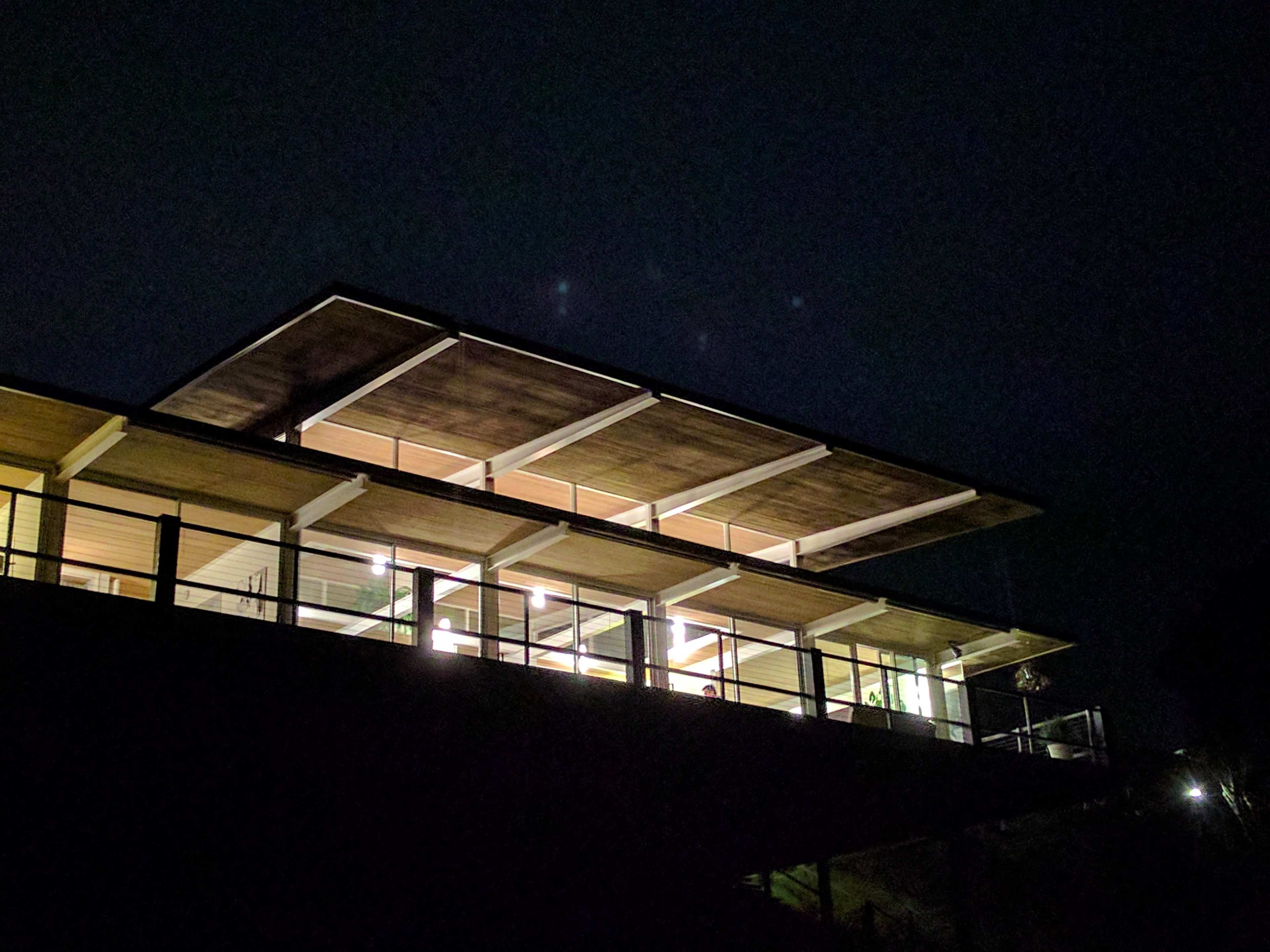 A modern building with a flat roof and large glass windows is illuminated at night.