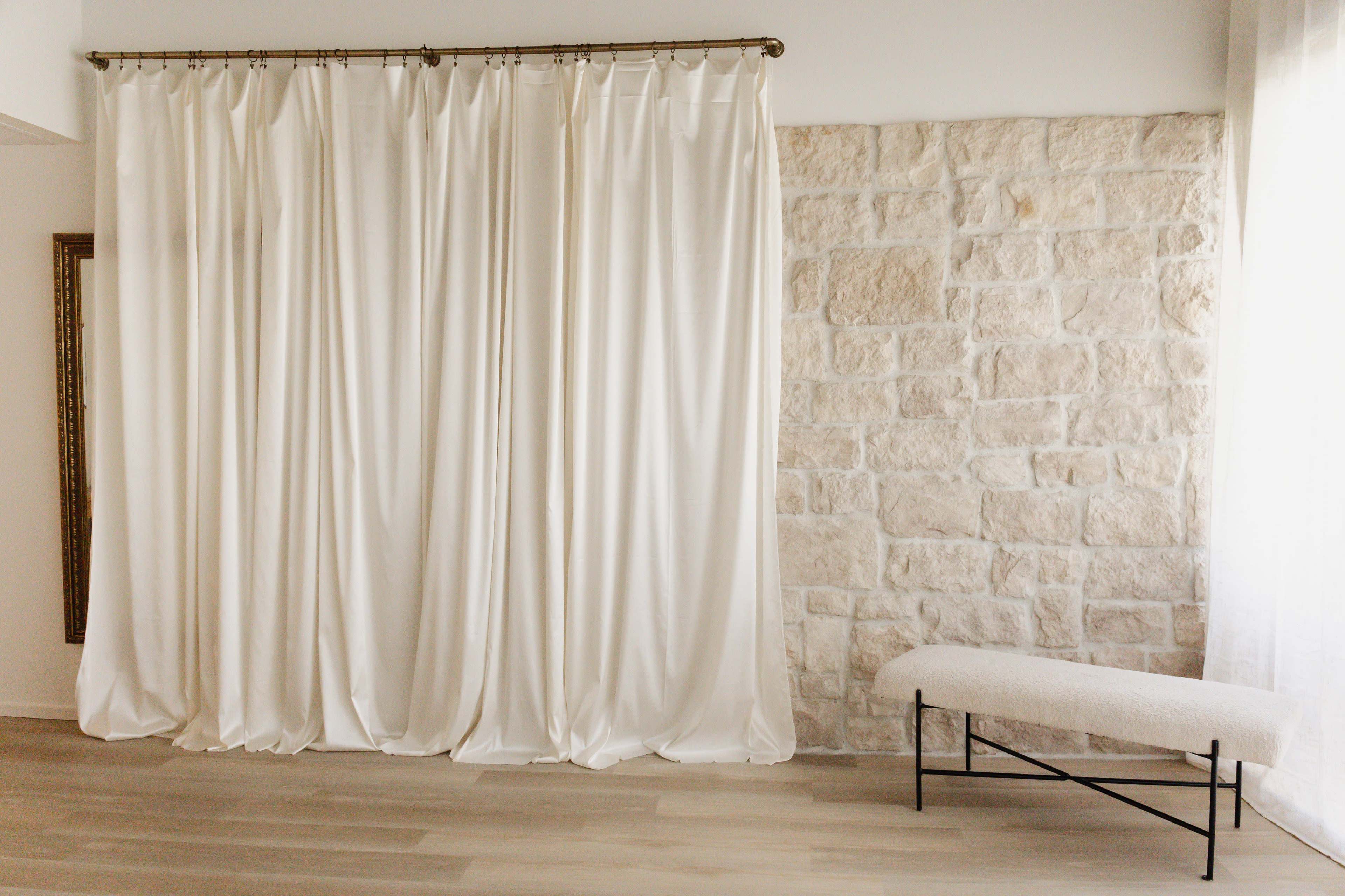 A room features a white curtain draped in front of a stone wall, with a padded bench positioned nearby.