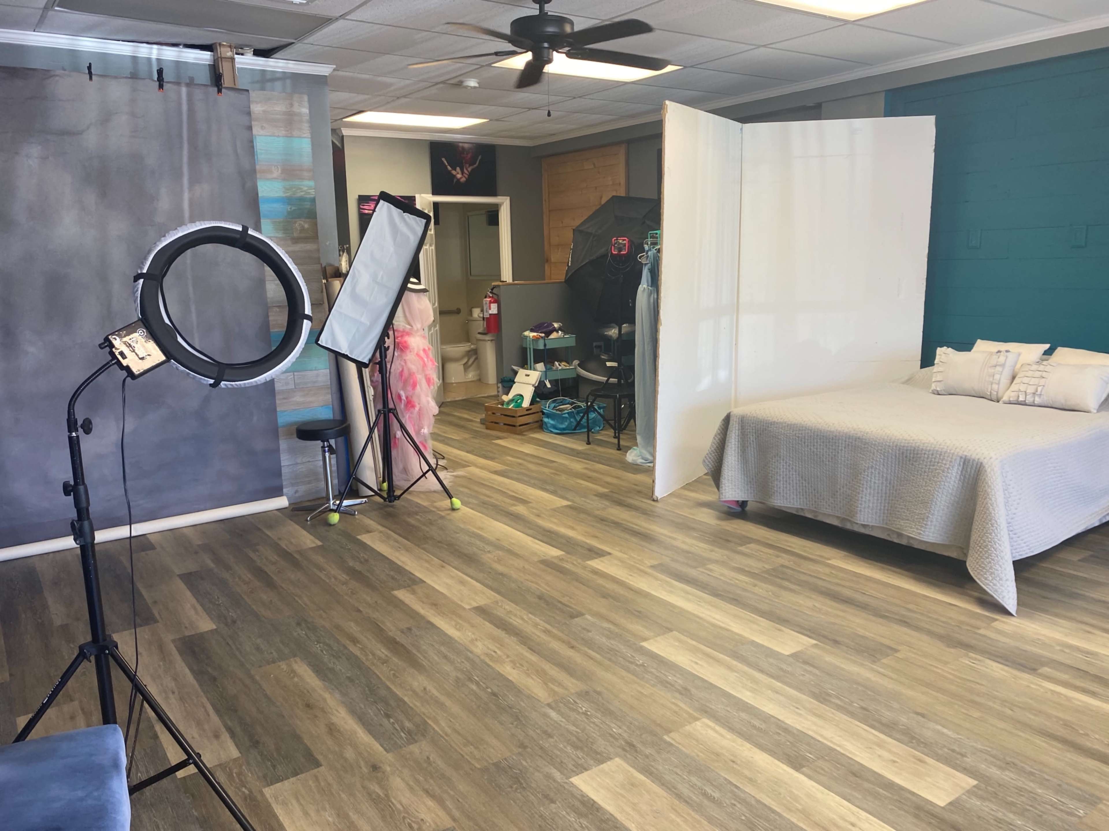 An indoor studio space with a bed, photography equipment, and a backdrop set up against a lightly colored wall.