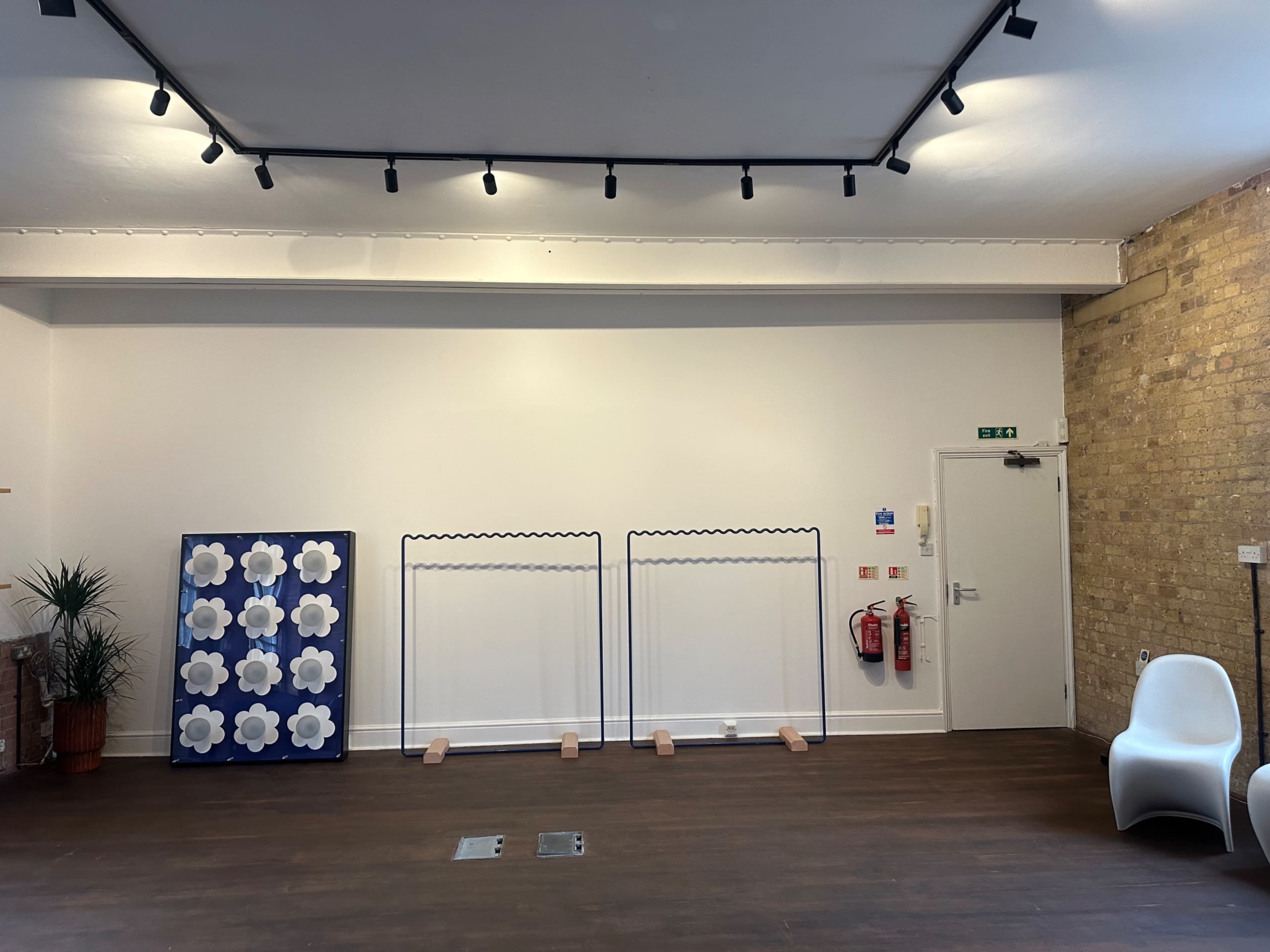 The image shows a spacious room with a blank white wall, two movable frames, a large blue and white decorative panel, and a white chair.