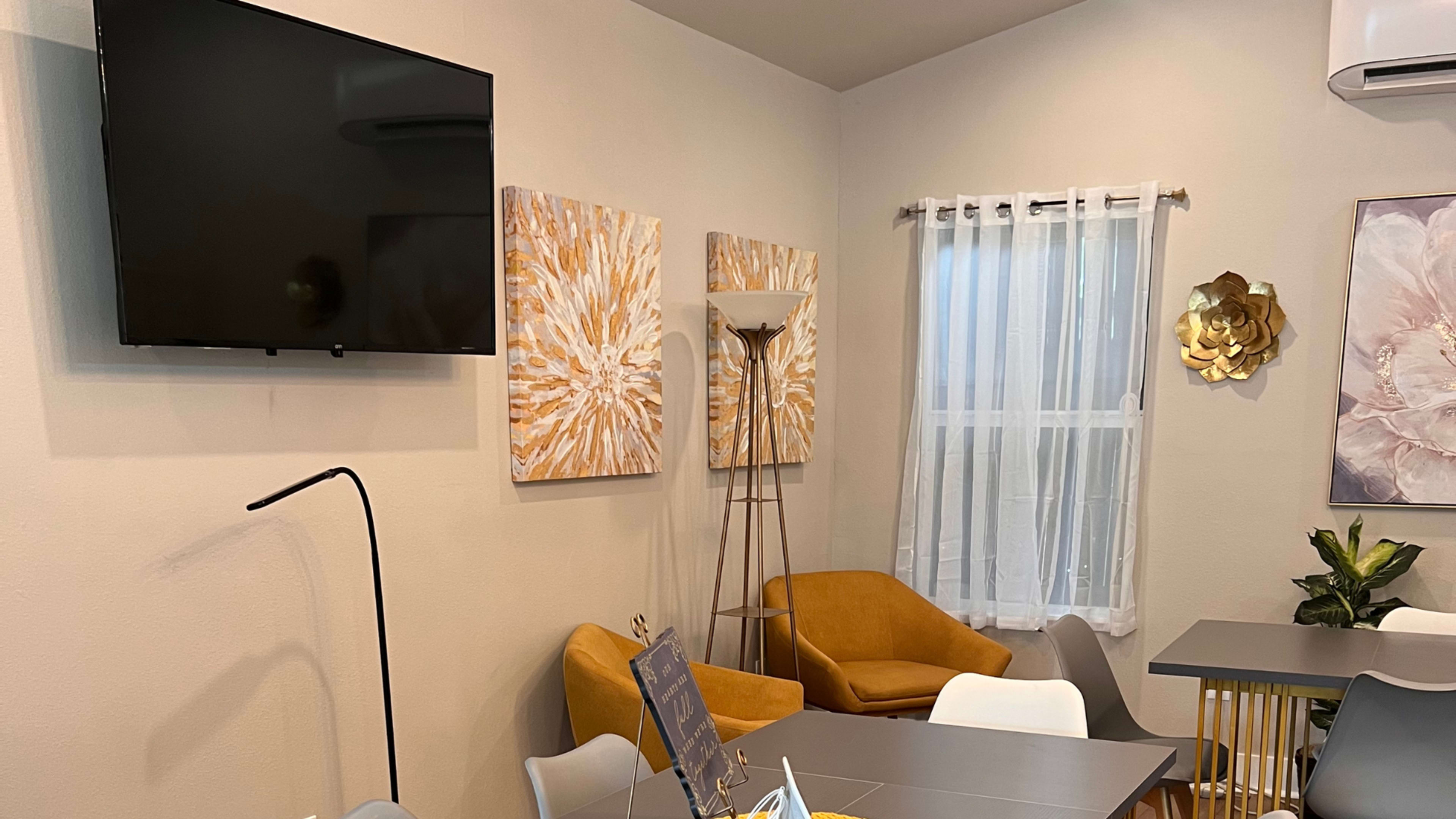 A modern interior space featuring a television mounted on a light-colored wall, two abstract paintings, and a mix of yellow and white furniture.