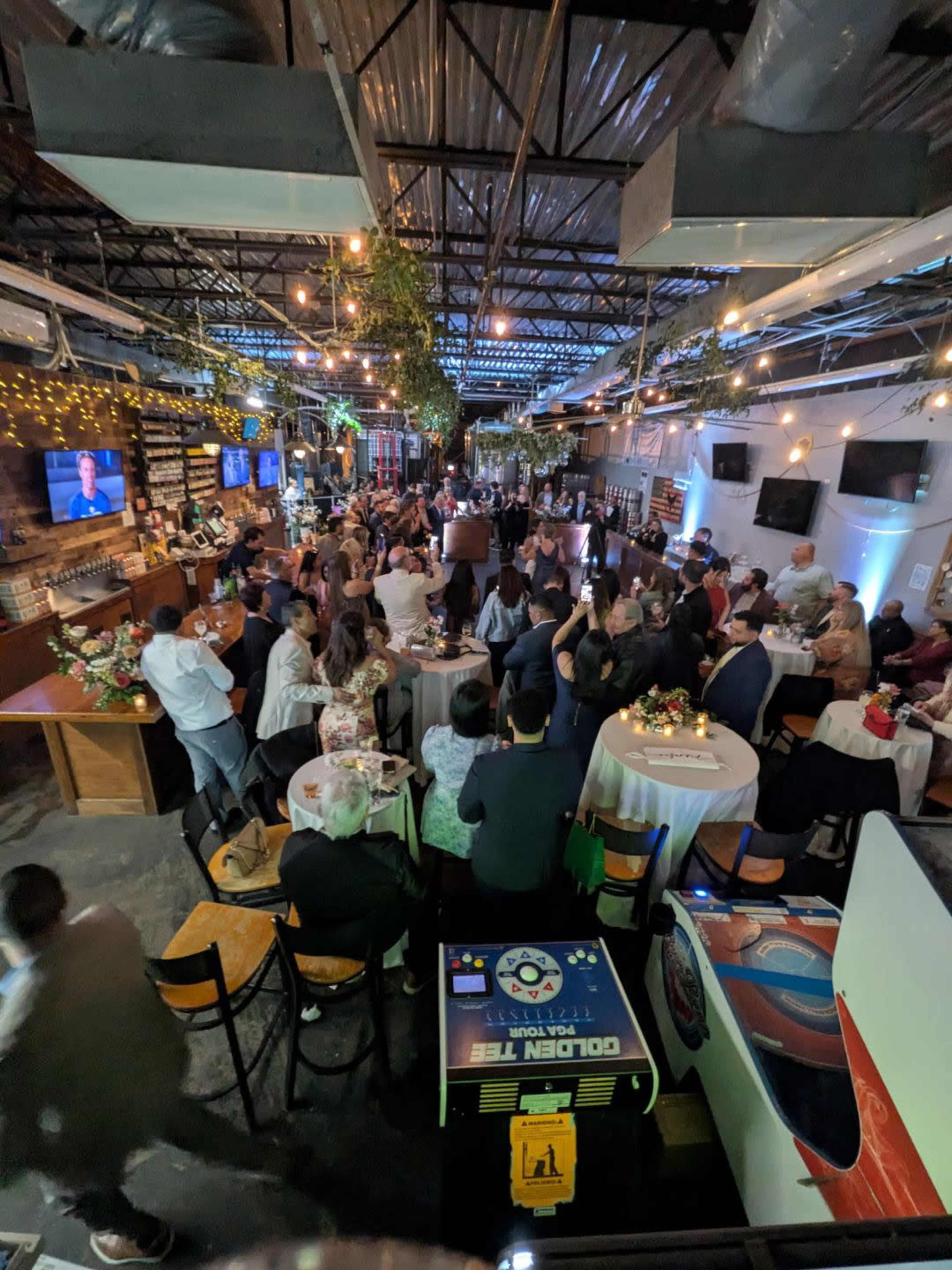 A crowded venue with guests seated at tables, socializing and enjoying the atmosphere under string lights.
