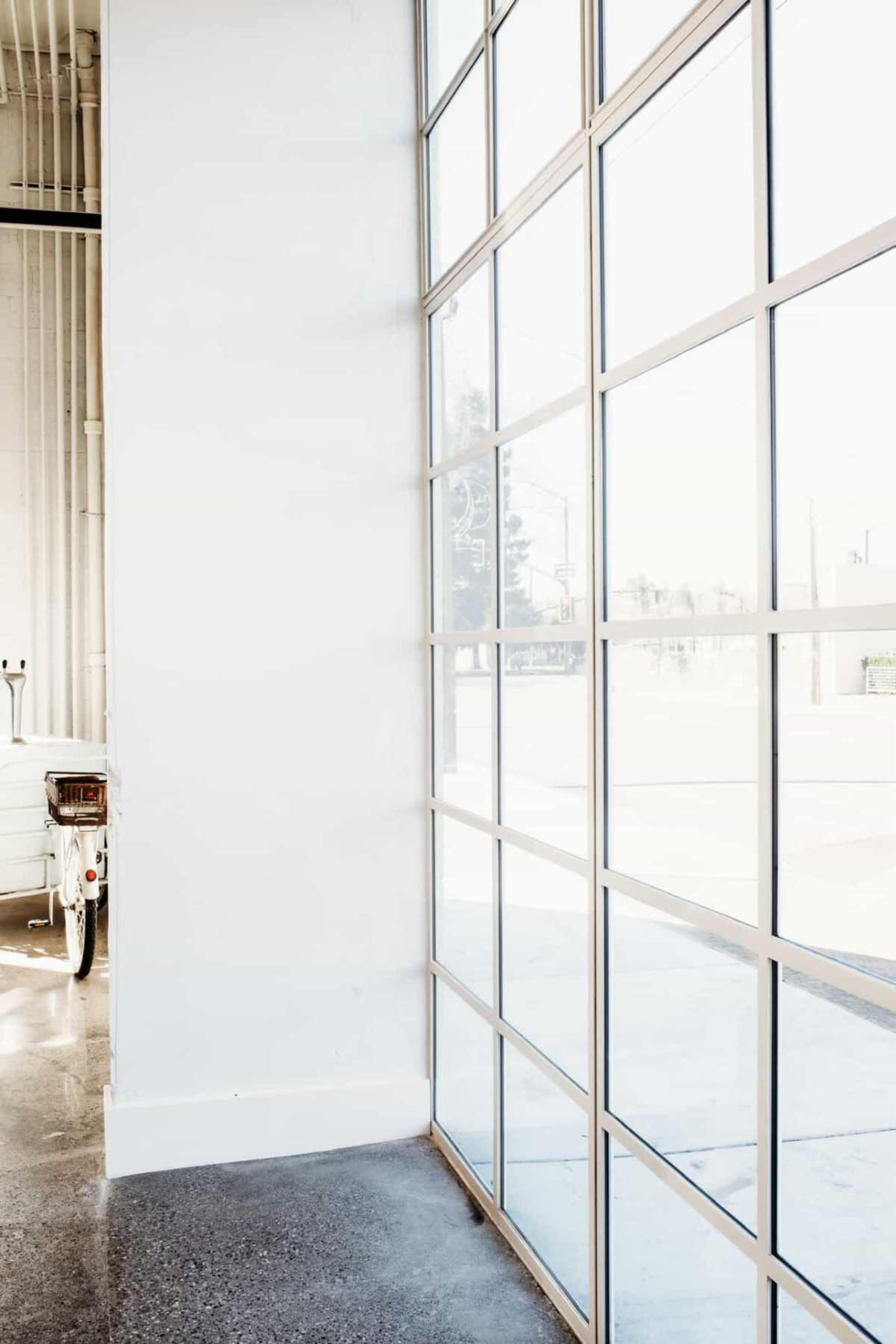 The image shows a large grid window in a minimalist room with light-colored walls and a reflection of the outside street.