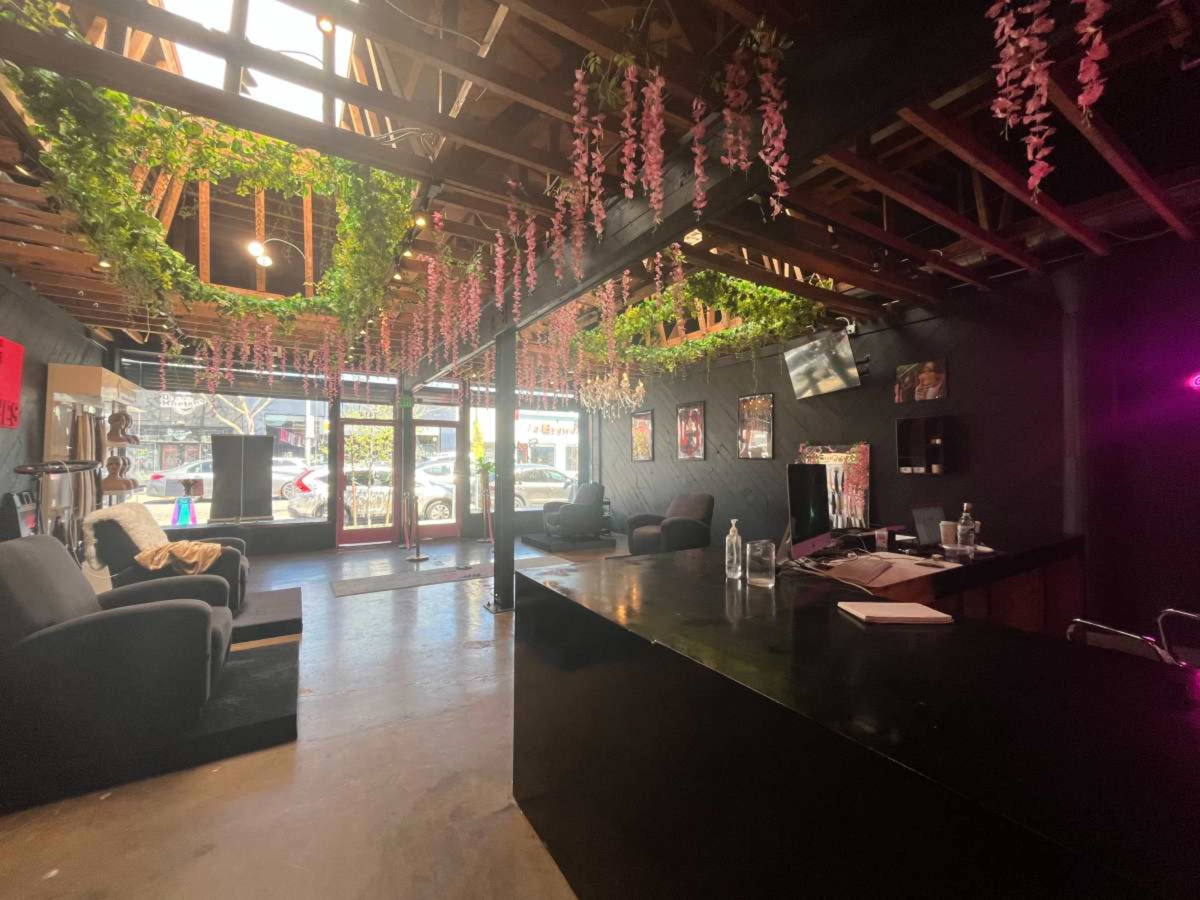 The image shows a modern interior space with seating arranged around a reception counter, featuring greenery and decorative elements hanging from the ceiling.
