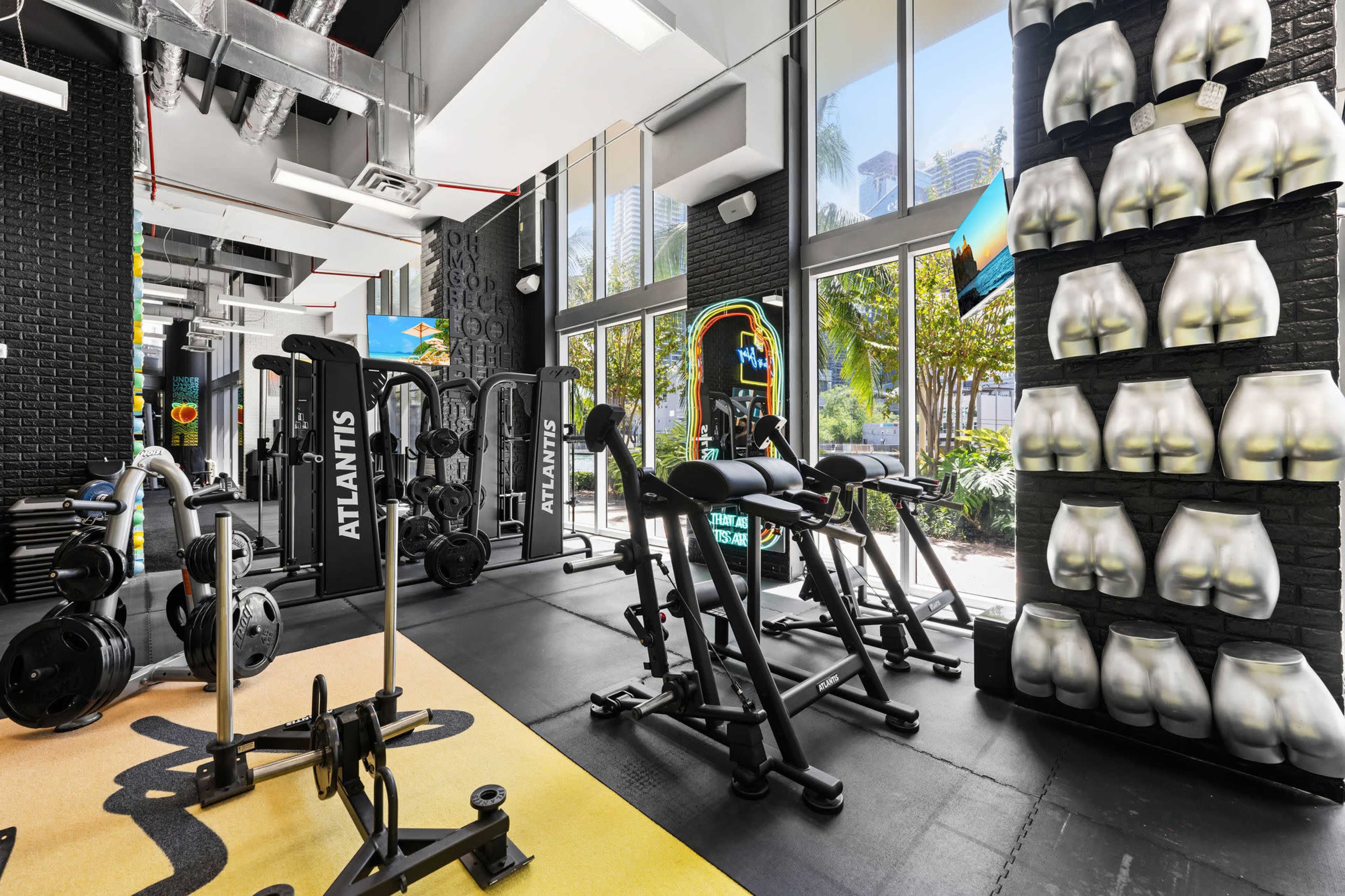 A modern gym with various weightlifting equipment and a wall display featuring molded exercise figurines.
