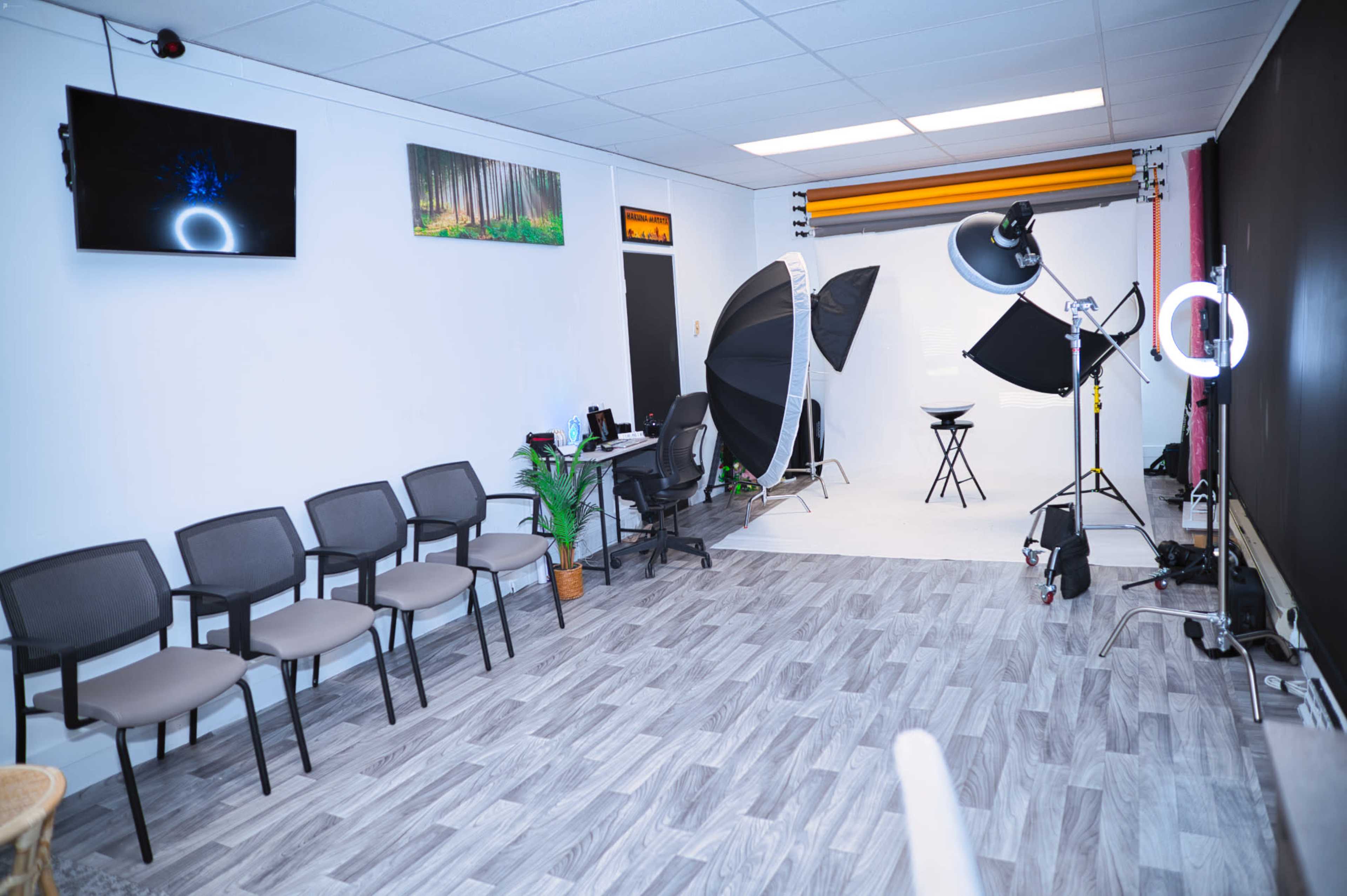 A photography studio with a seating area, two large softboxes, a backdrop setup, and a chair in the center.