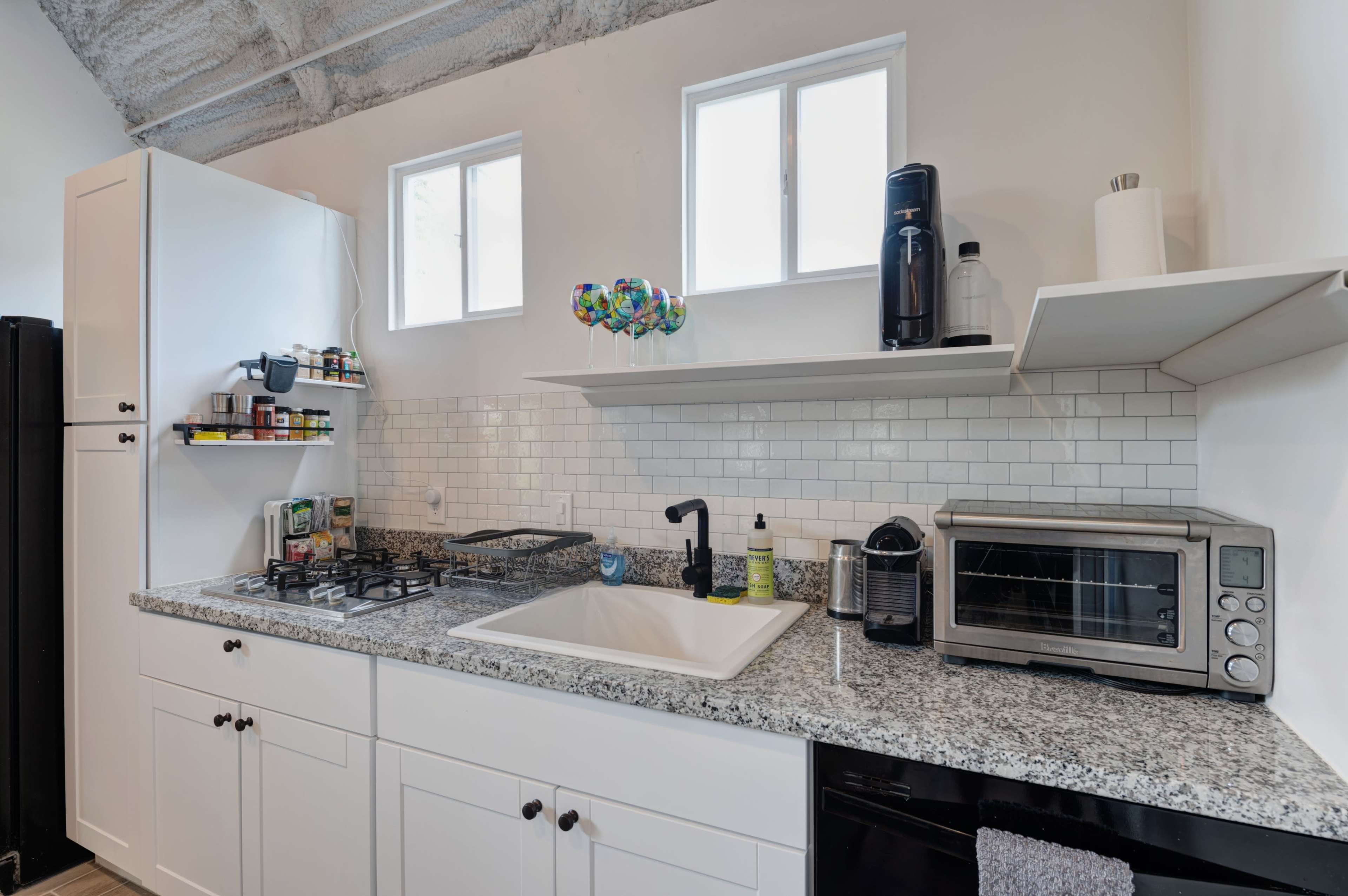 A modern kitchen features a granite countertop with a sink, gas stove, microwave, and shelves holding various kitchen items and decor.