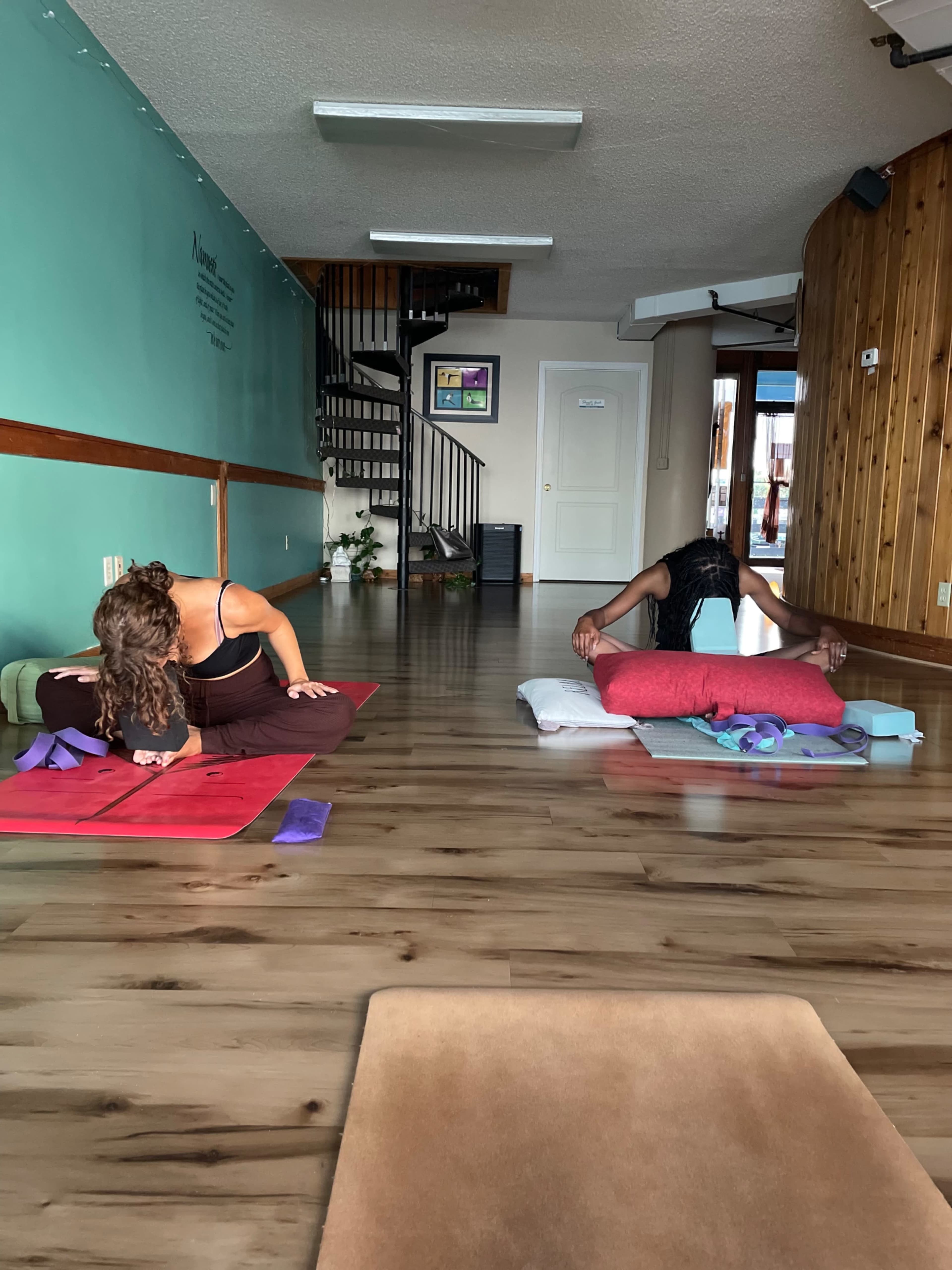 Two individuals practice yoga in a peaceful studio setting, each positioned on their mats with different poses.