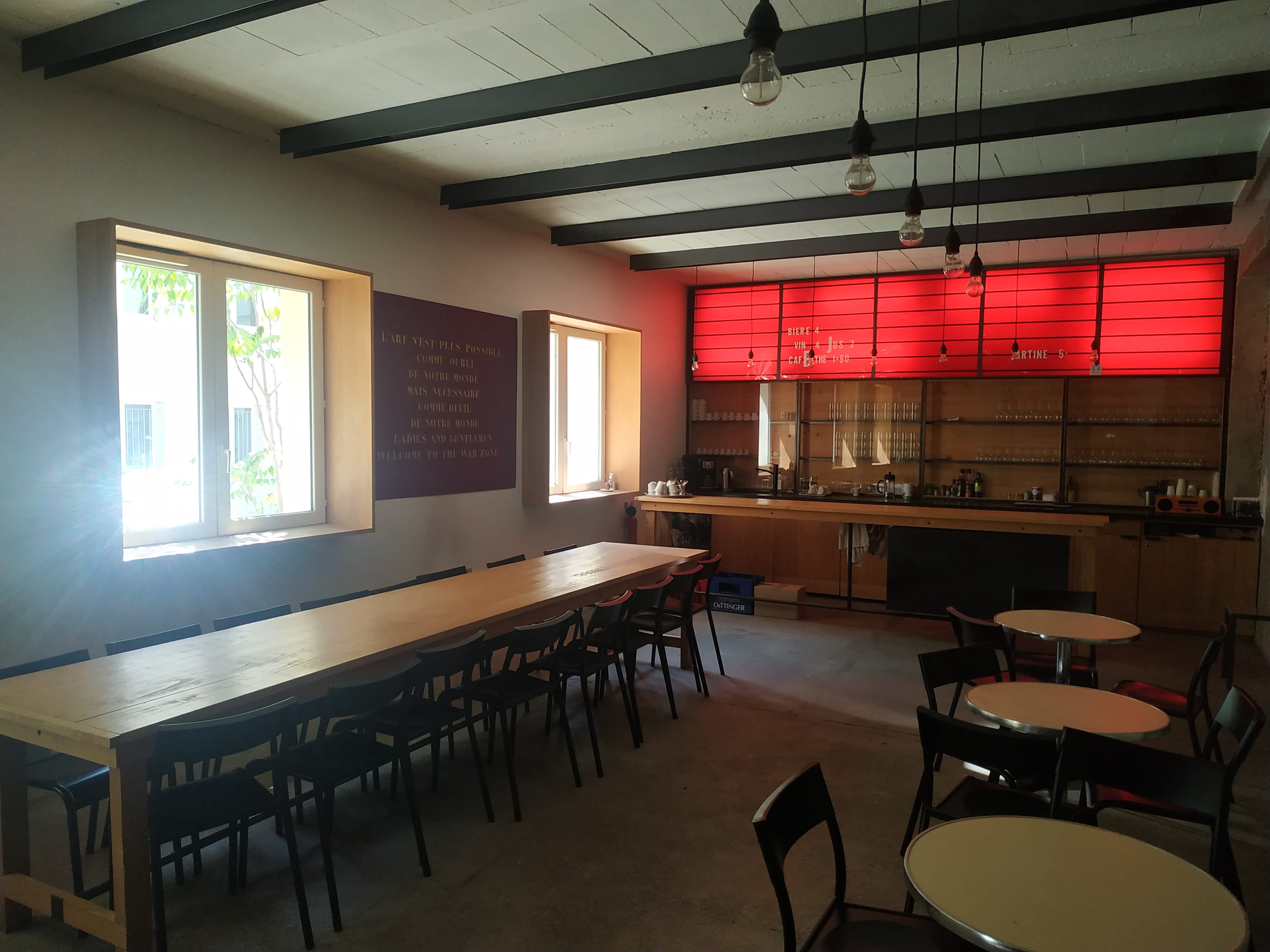 A spacious dining area with a long wooden table, chairs, and a kitchenette featuring a red backlit panel.