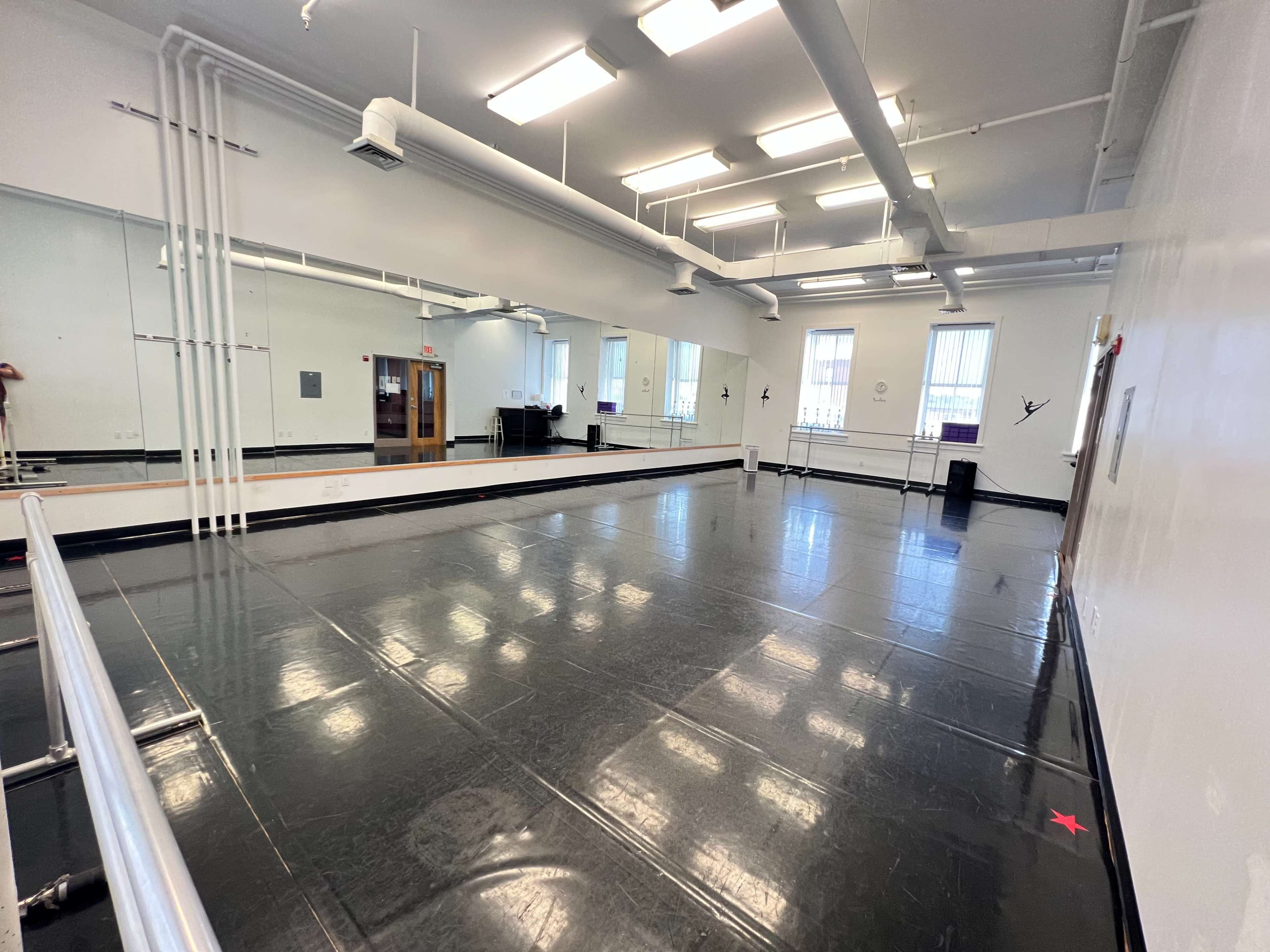 A spacious dance studio with large mirrors, a ballet barre, and polished black floors.