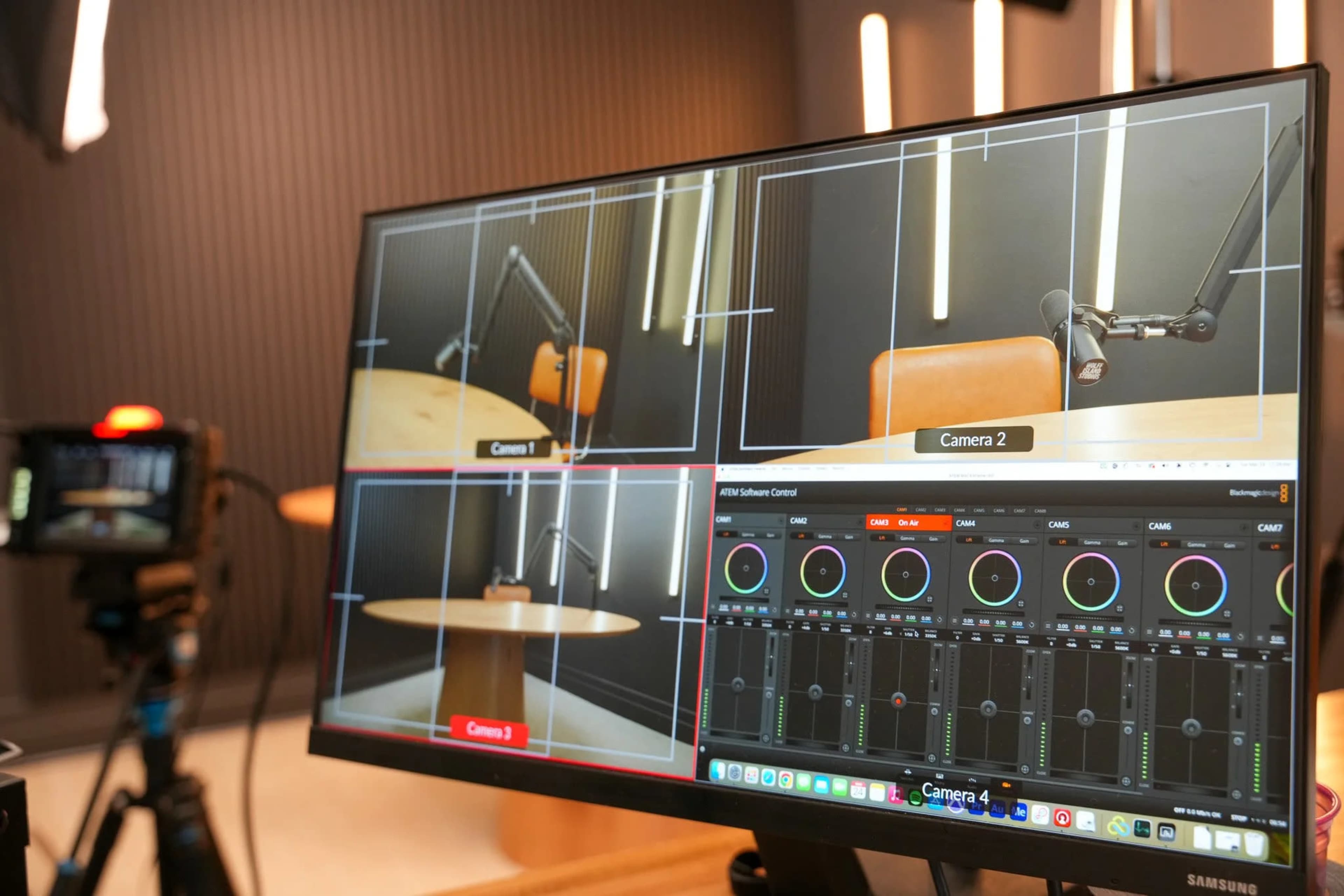 The image shows a computer monitor displaying a multi-camera control interface with three camera views and audio control sliders in a studio setup.