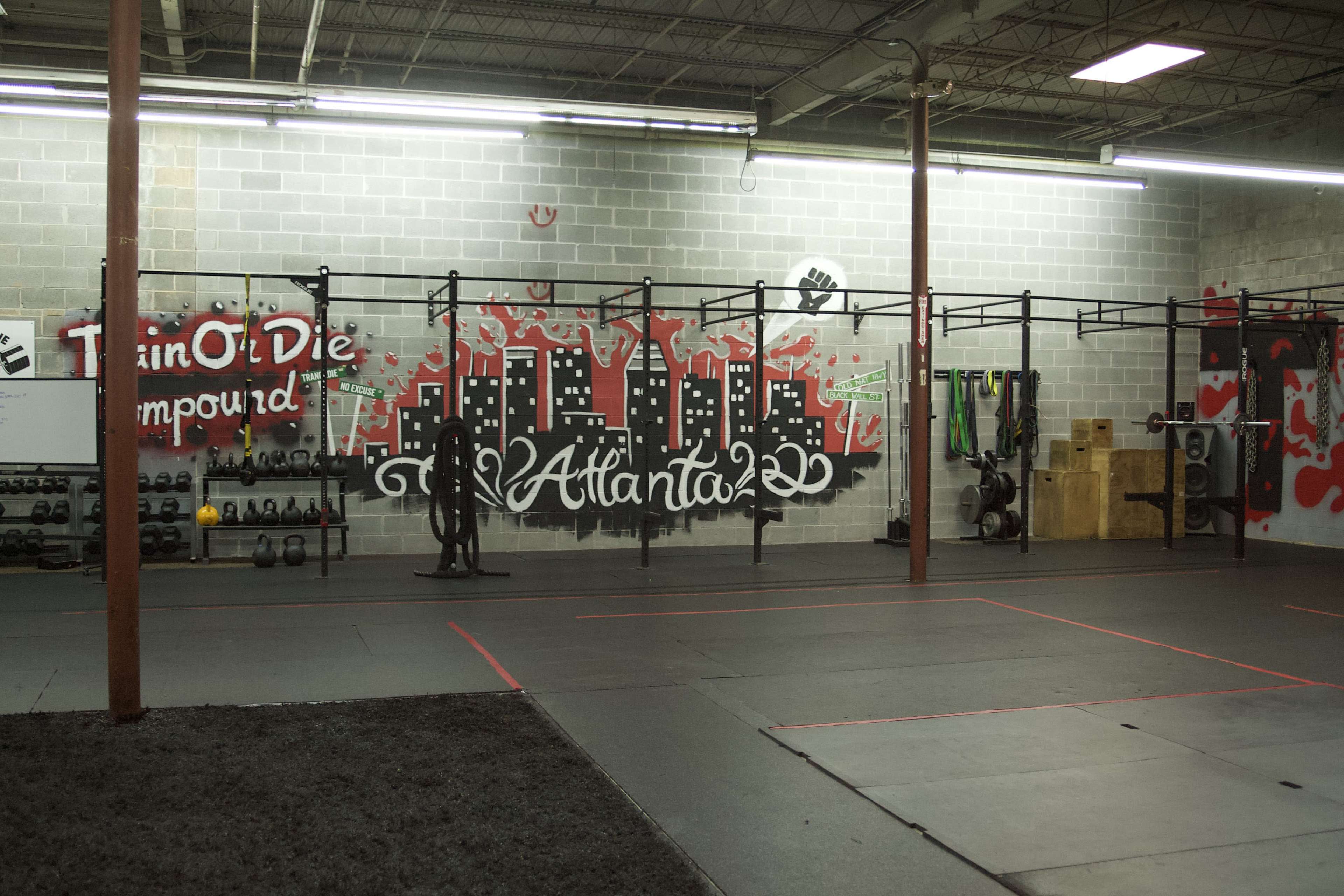The image shows a gym interior with weightlifting equipment and a mural depicting a city skyline on the wall.