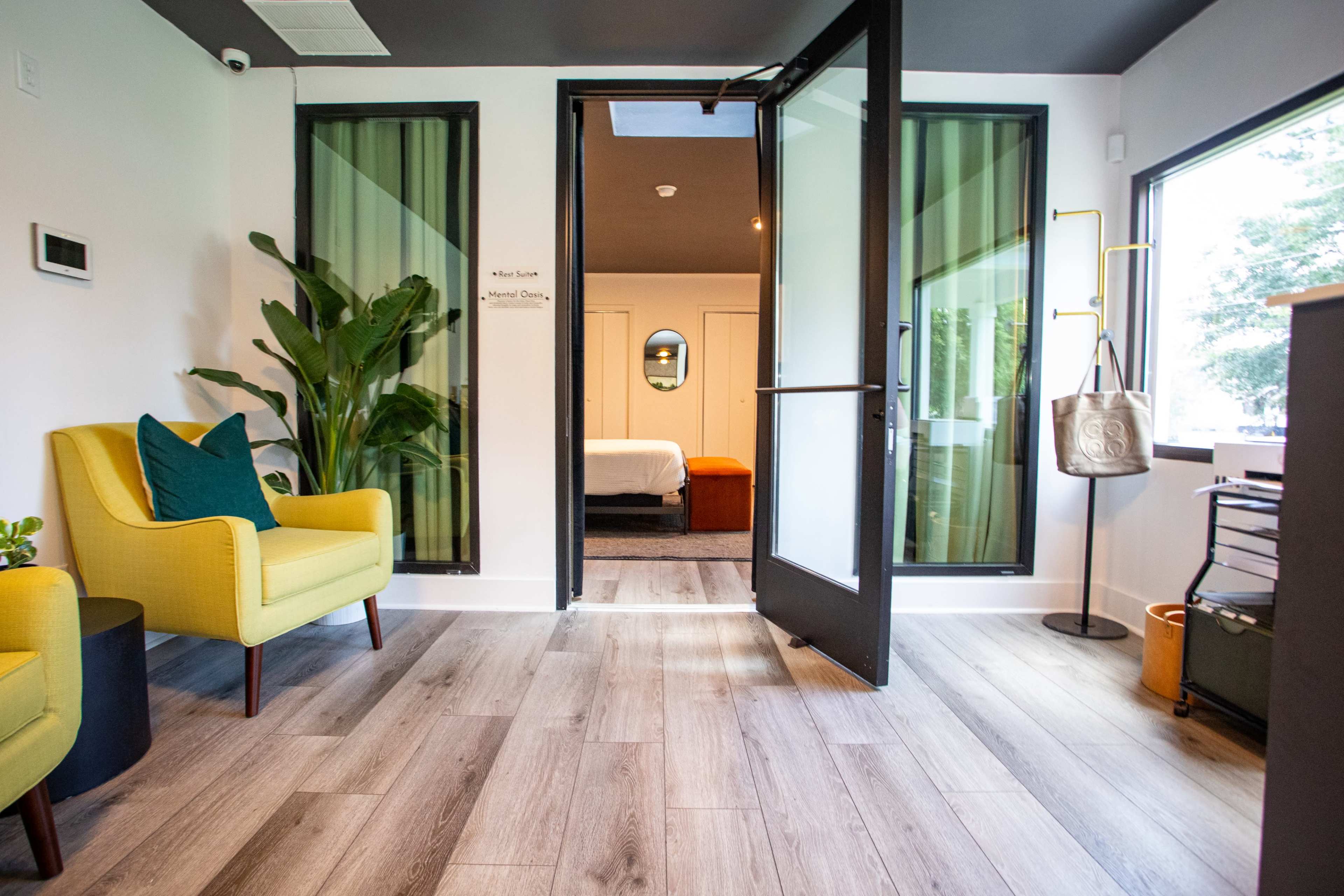 The image shows a modern reception area with two yellow chairs, a door leading to a room, and a potted plant beside the entrance.