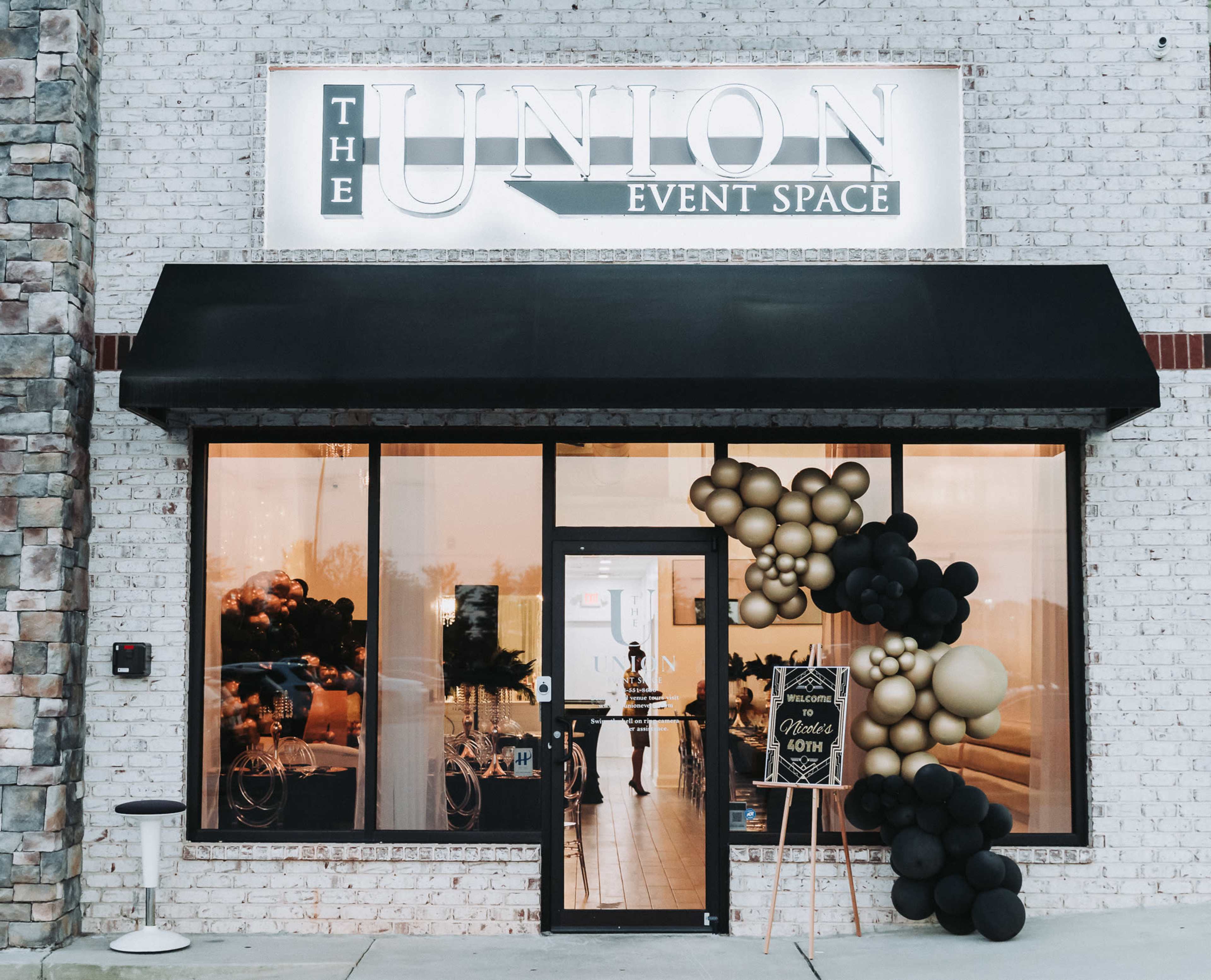 The entrance of "The Union Event Space," featuring a decorative sign, large windows, and a balloon arch in black and gold.