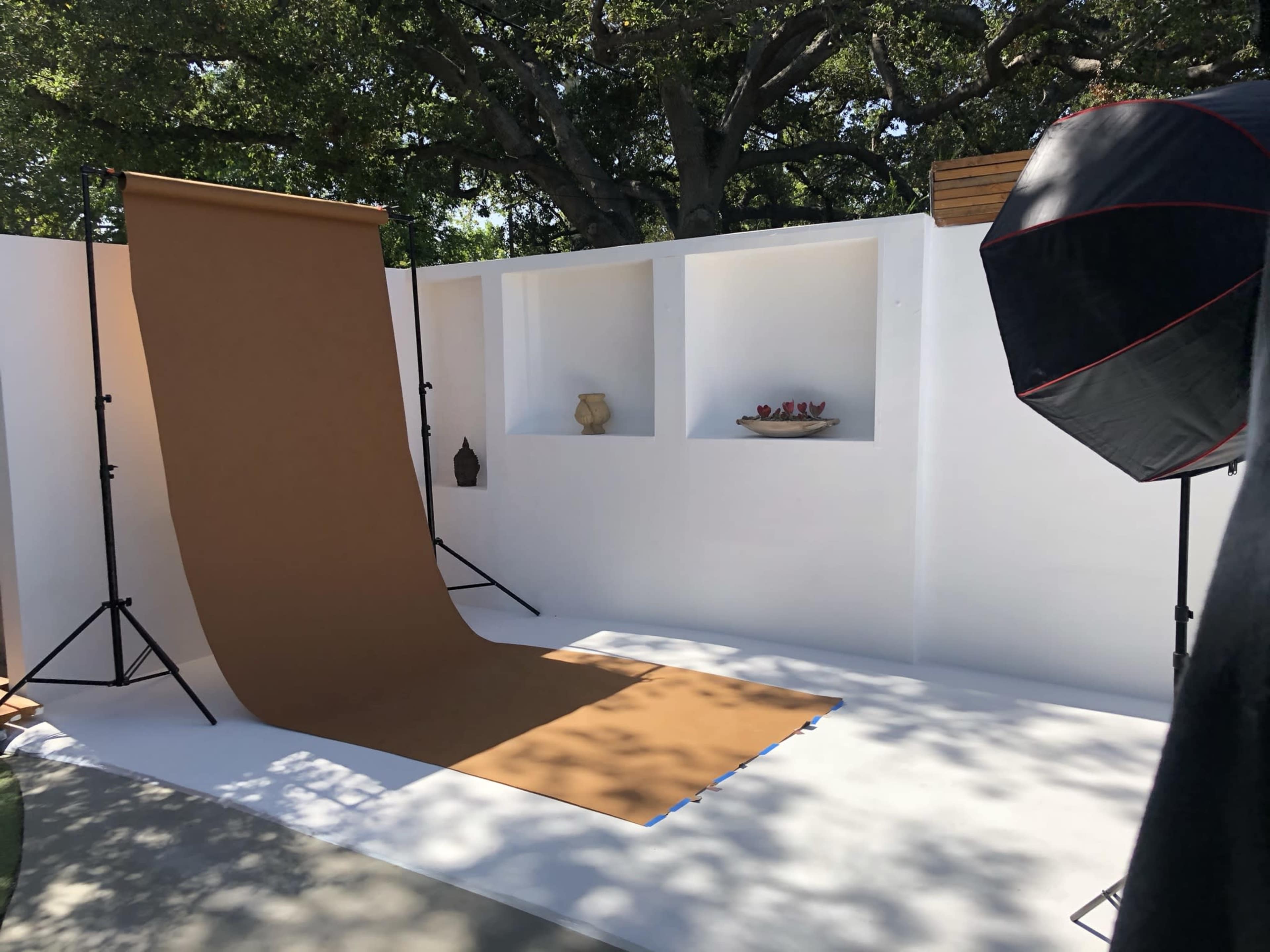 A photography setup featuring a brown backdrop, softbox lighting, and a white textured wall with decorative shelves.