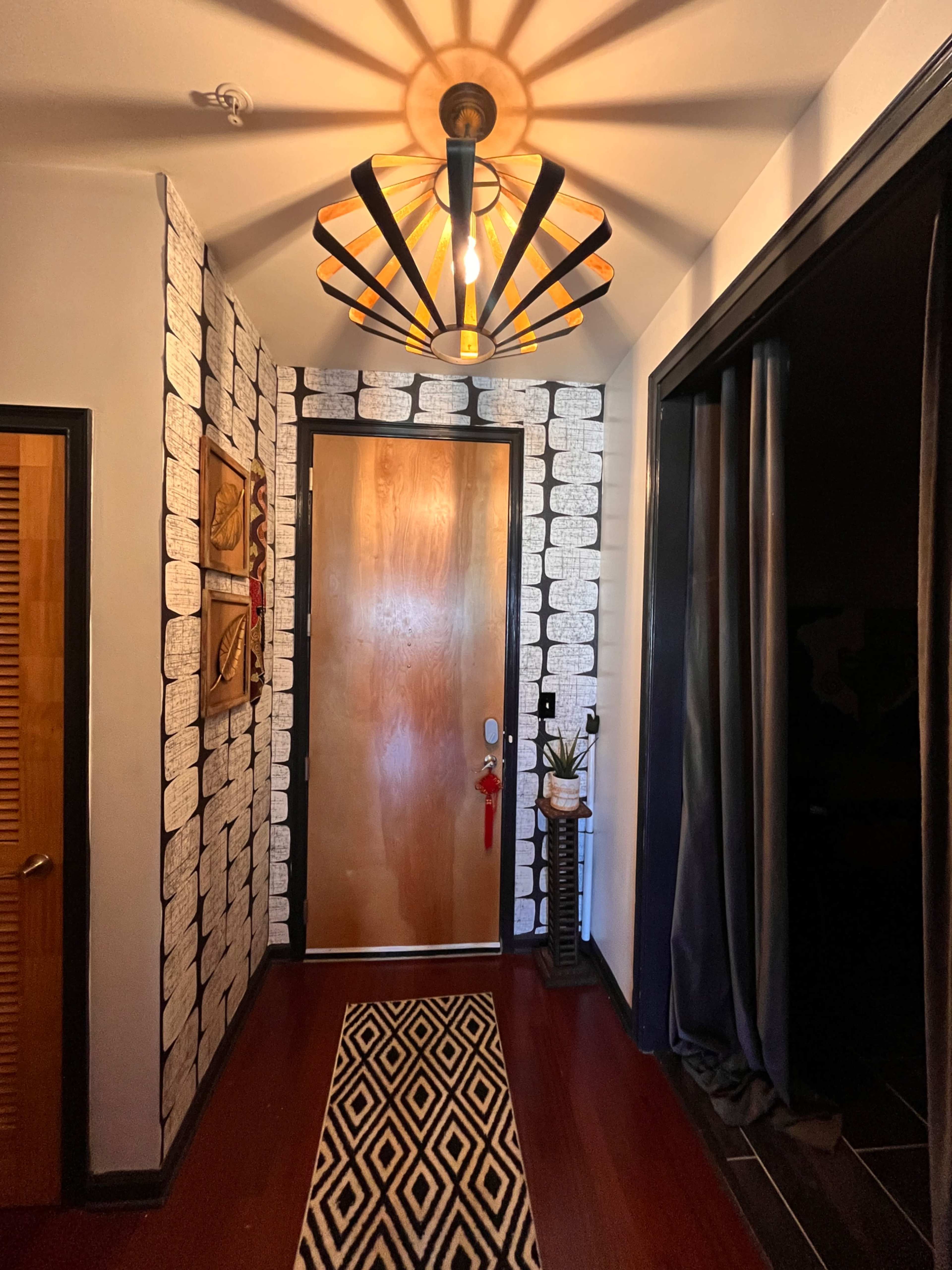 A narrow hallway features a wooden door, a patterned rug, and a decorative light fixture casting shadows on the walls.