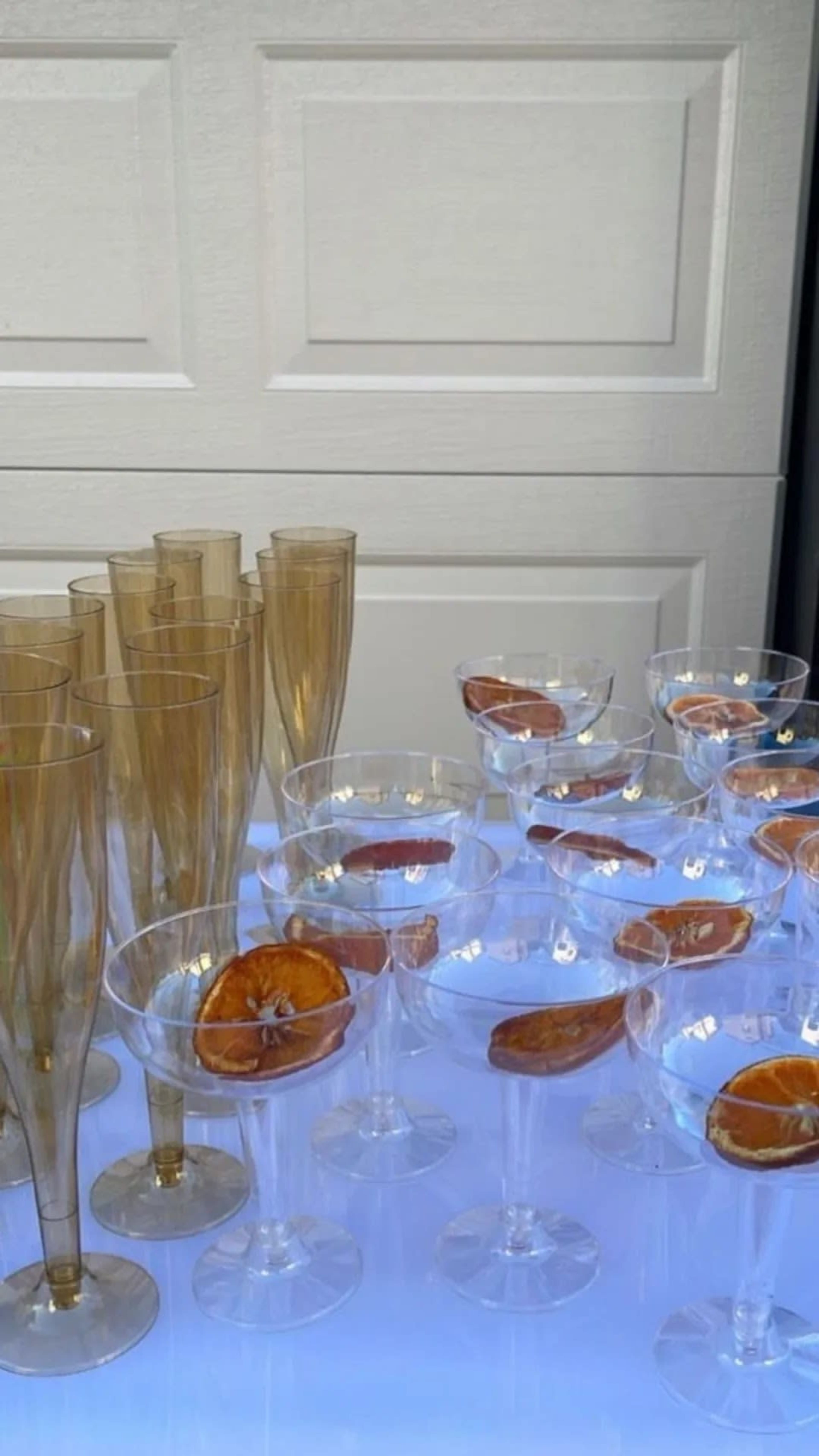 A collection of clear and gold-tinted glasses arranged in rows, some filled with dried orange slices, on a white surface.