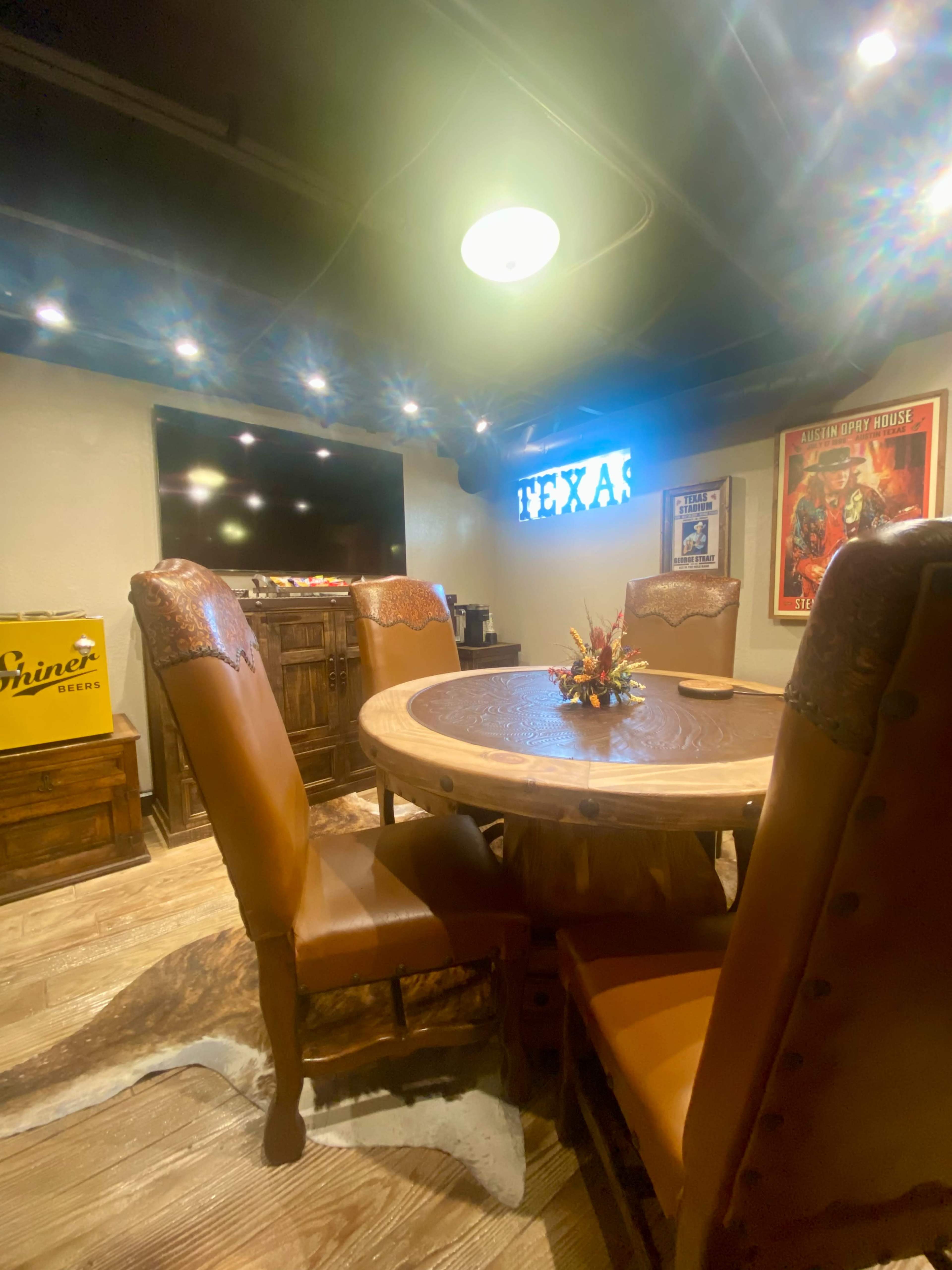 A rustic dining room with a round wooden table, leather chairs, and a decorative centerpiece, illuminated by overhead lighting.