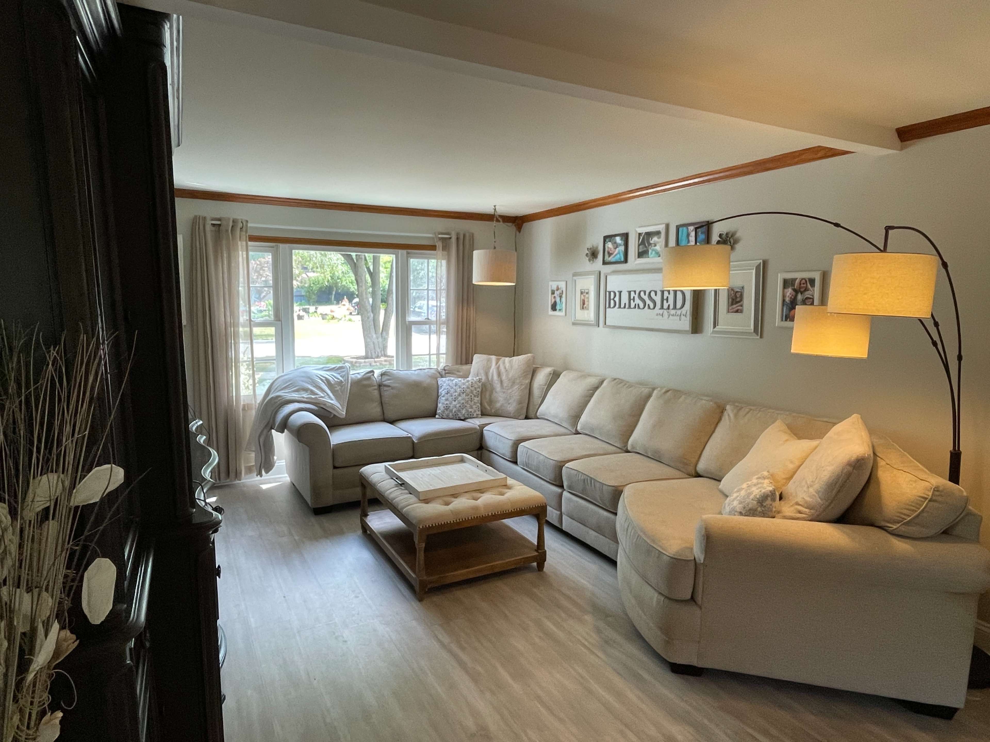 A bright living room featuring a large beige sectional sofa, a coffee table, and a series of framed photos on the wall, with windows letting in natural light.