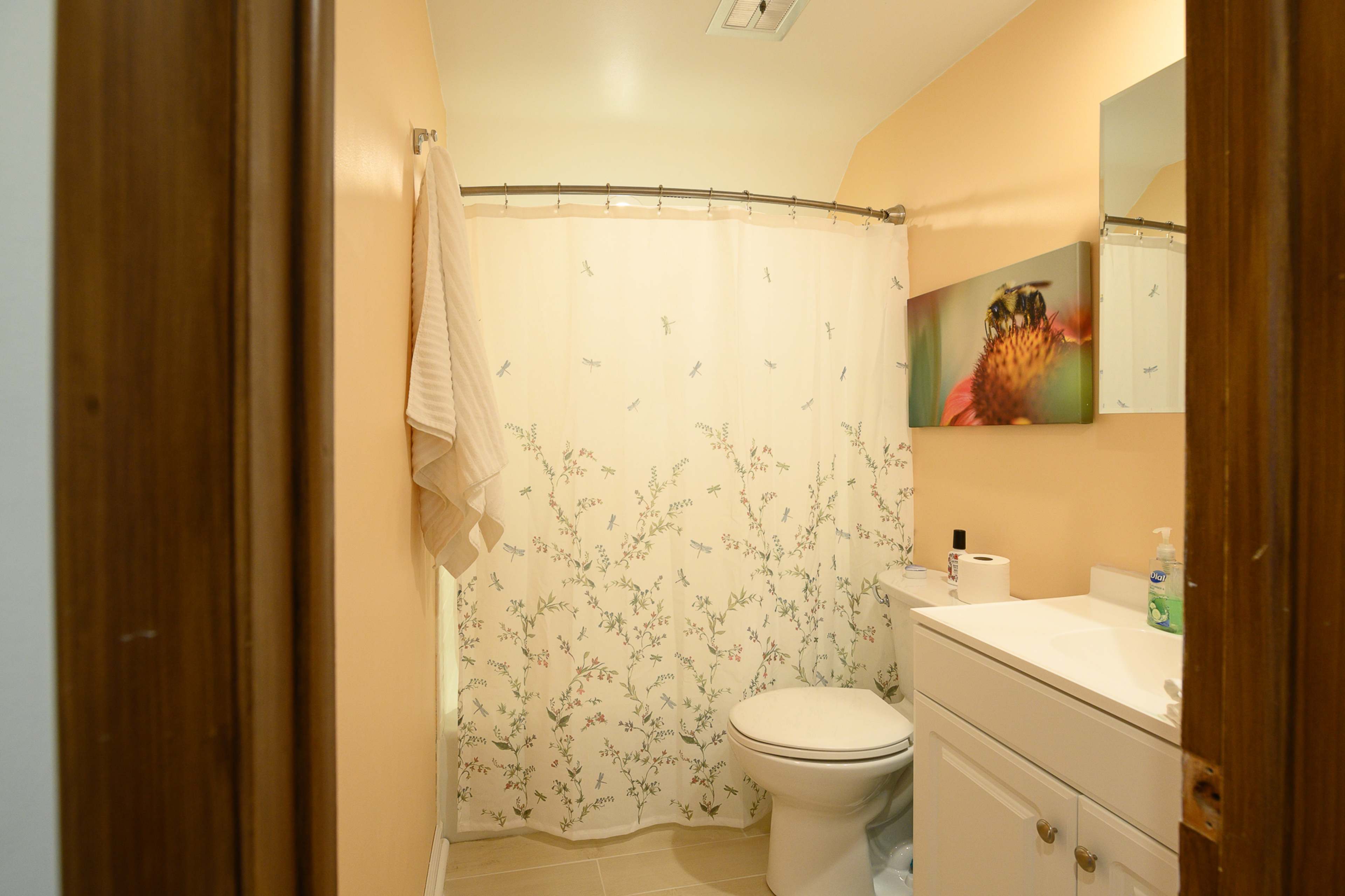 A small bathroom features a shower curtain with floral designs, a white toilet, and a sink with a mirror above it.
