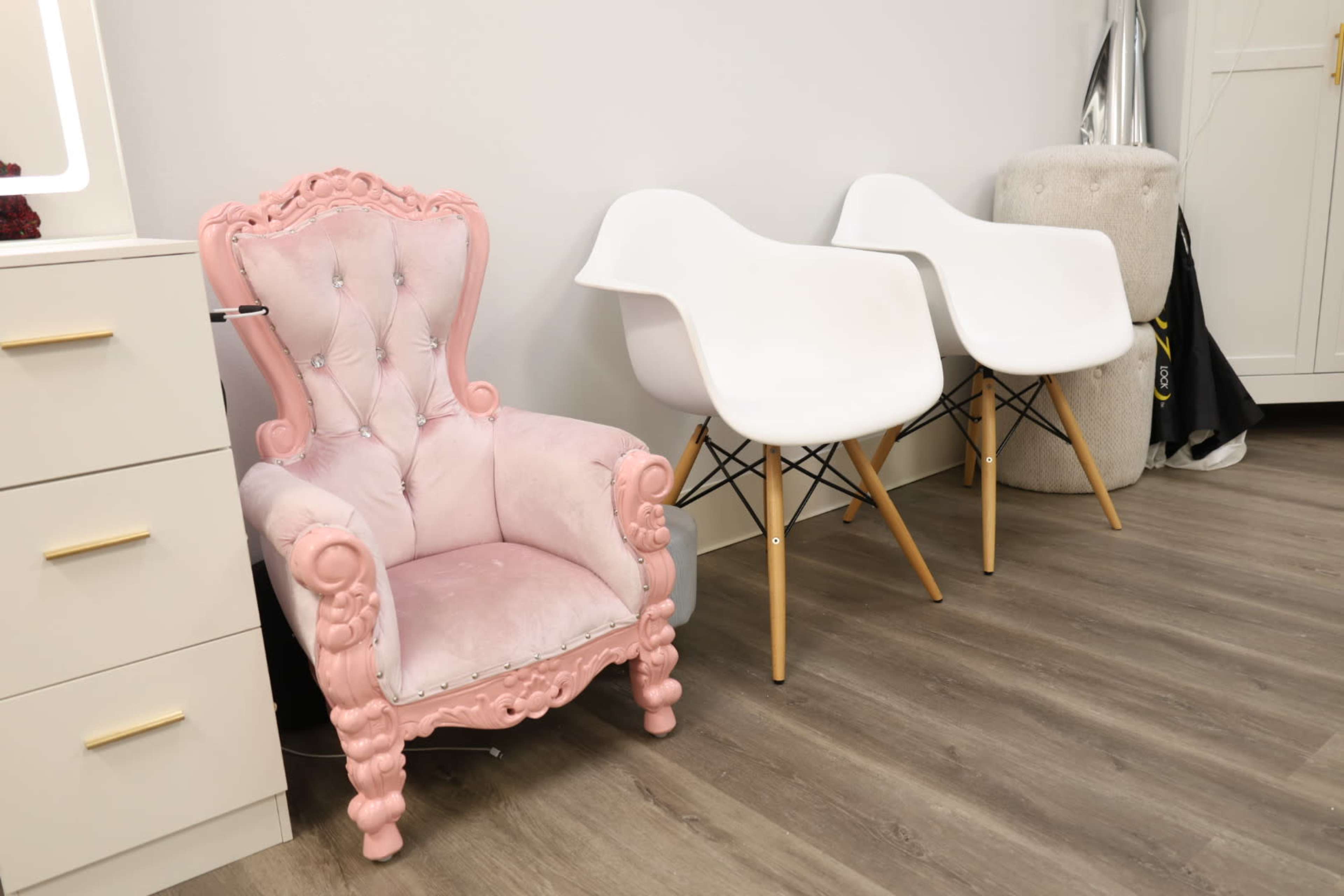 A pink upholstered chair with ornate detailing sits beside two modern white chairs on a wooden floor.