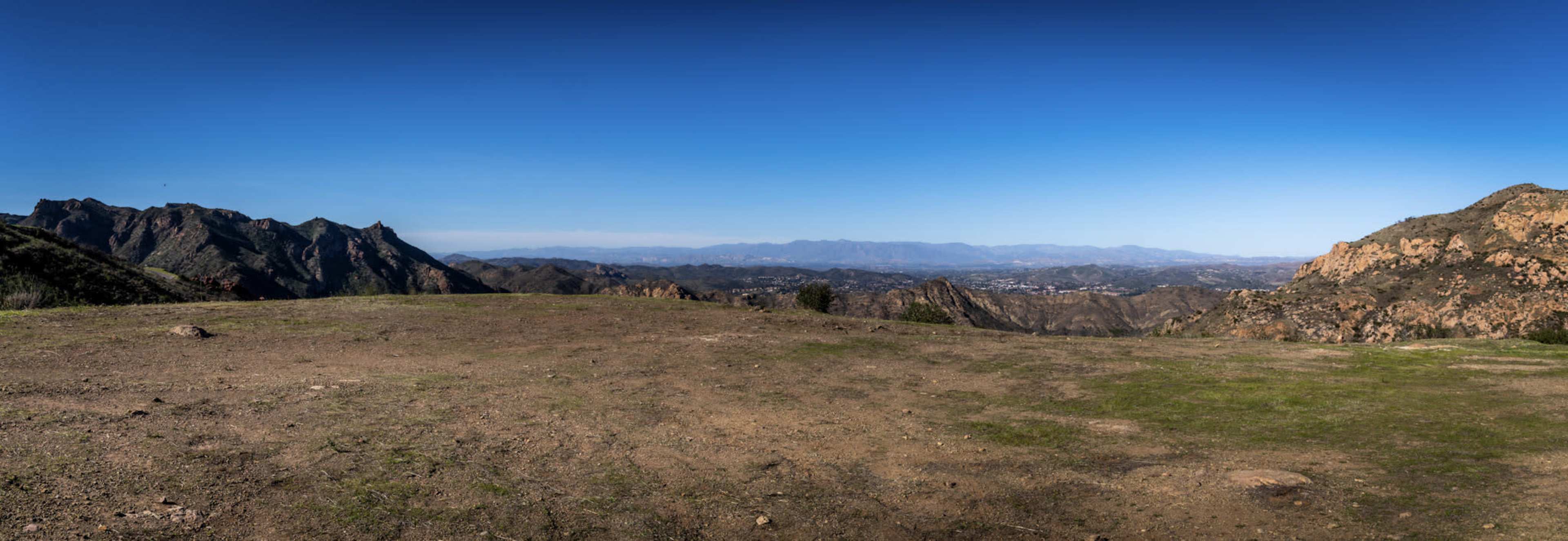 A panoramic view of a mountainous landscape with a clear blue sky and a valley in the distance.