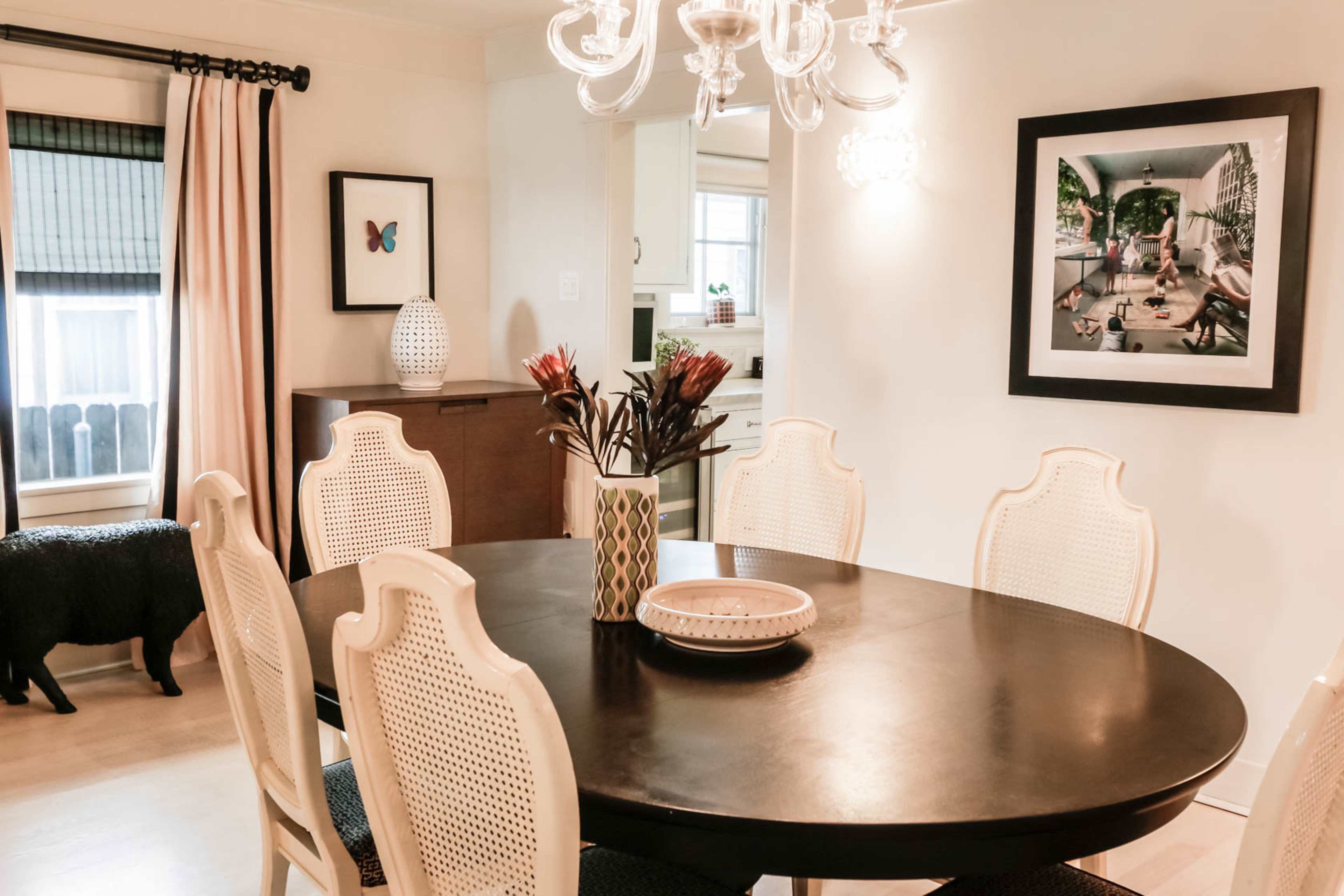 A round dining table is set in a well-lit room with a chandelier, surrounded by eight chairs, with a decorative vase at its center.
