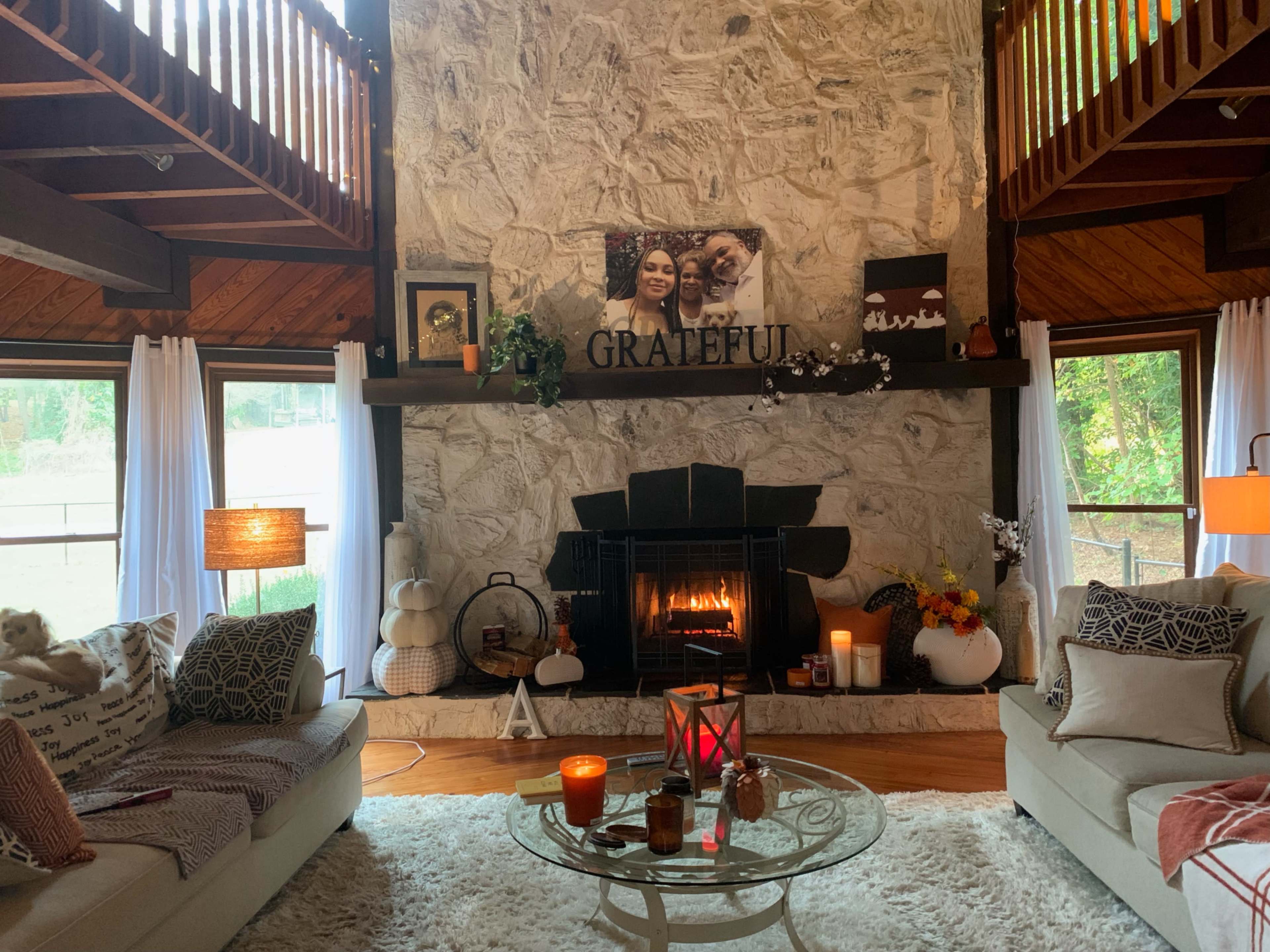 The image shows a cozy living room with a stone fireplace, decorated with a "GRATEFUL" sign and various fall-themed decorations.