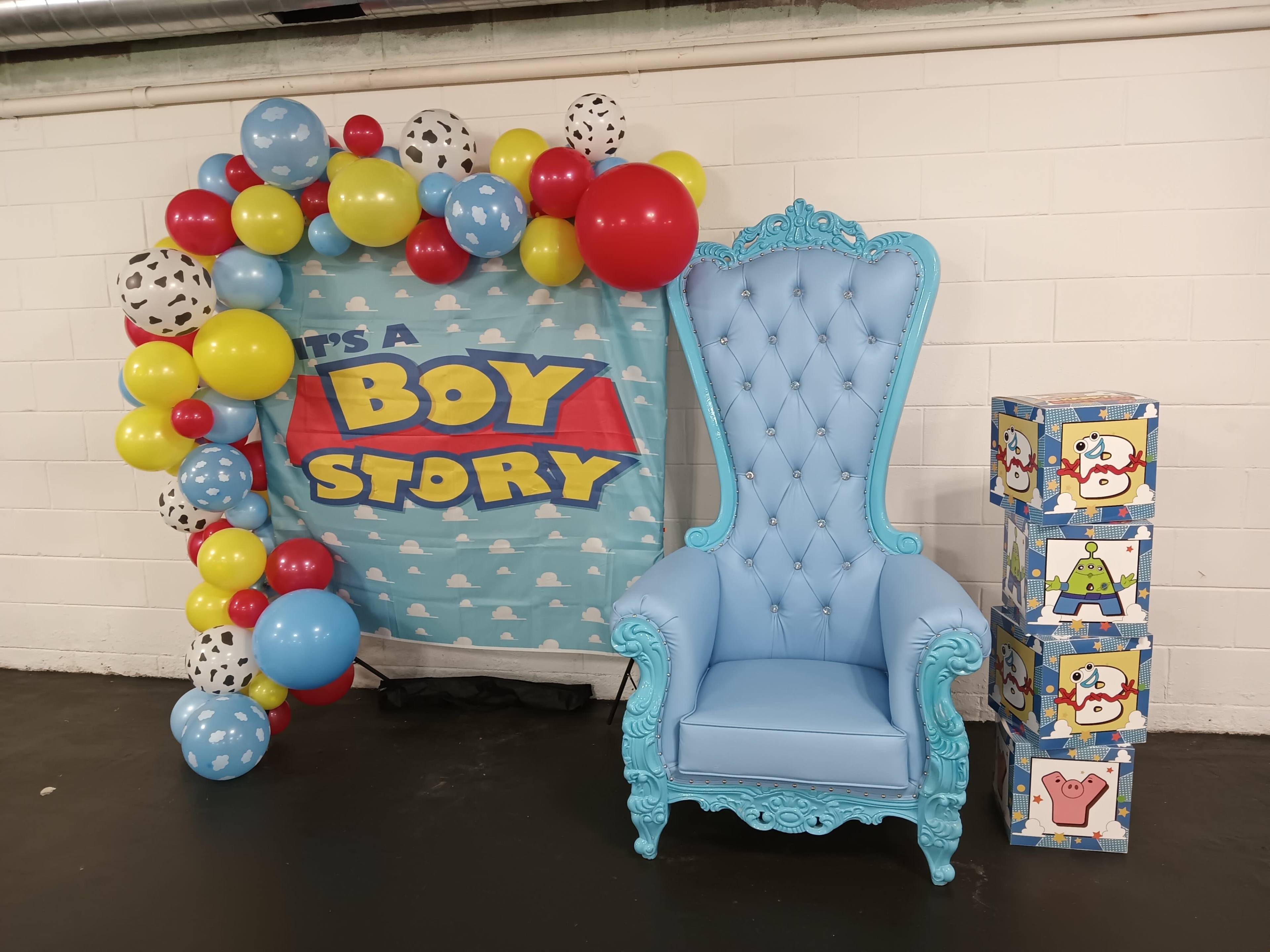 A blue chair, colorful balloons, and a backdrop that reads "It's a Boy Story," accompanied by decorative boxes with cartoon characters.