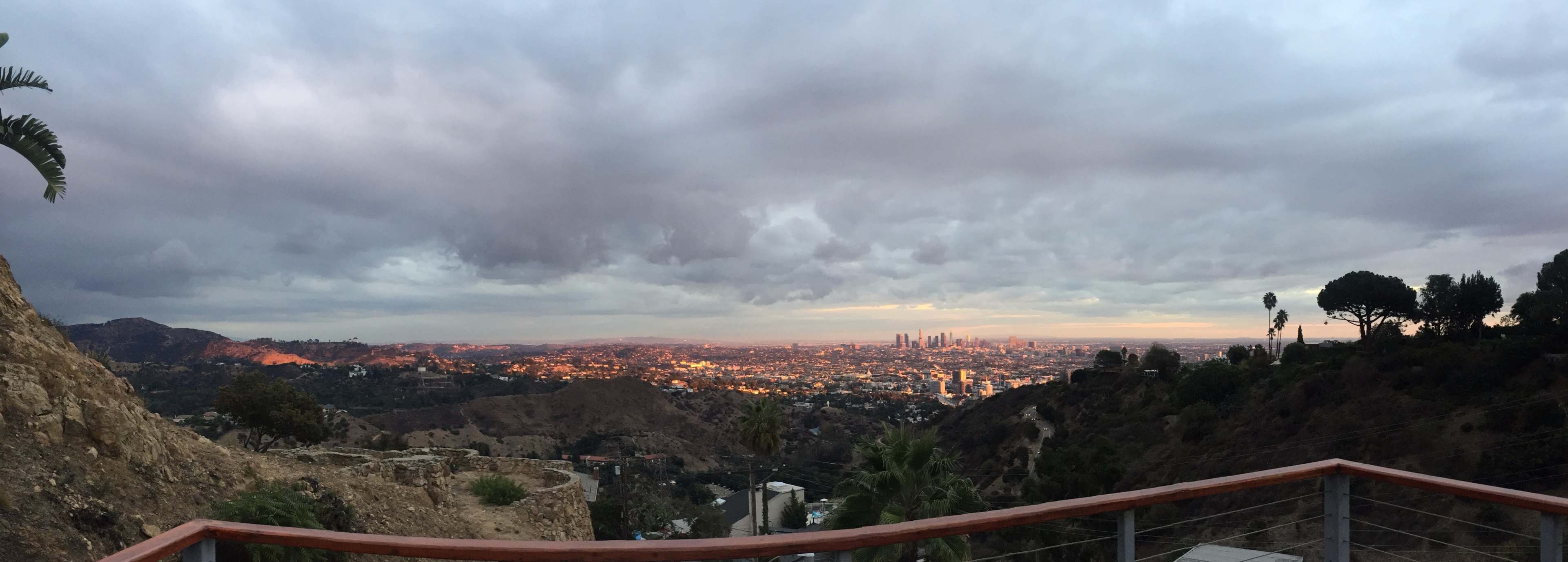A panoramic view captures the sprawling city of Los Angeles at dusk, with hills in the foreground and skyscrapers visible in the distance.