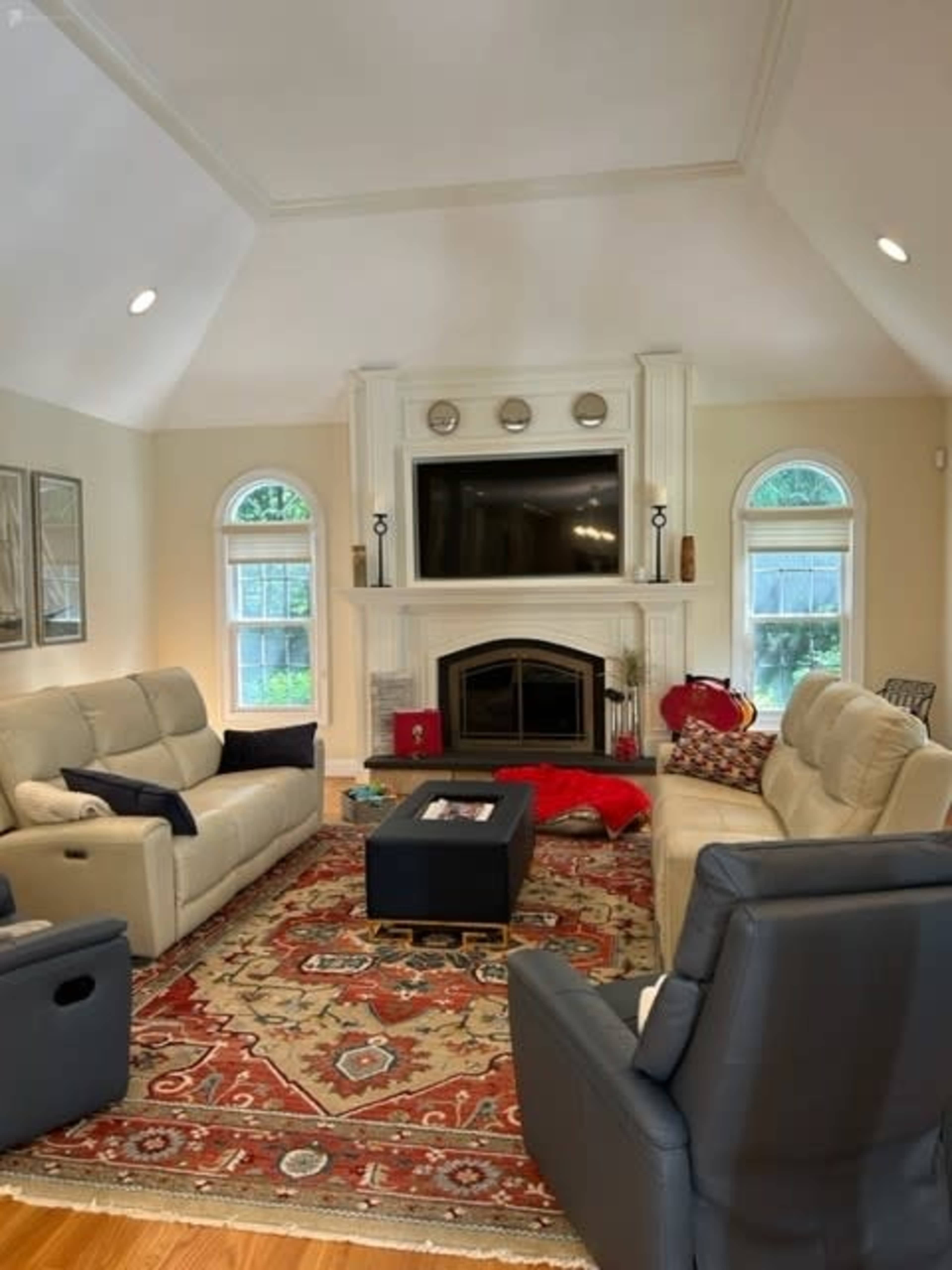 The living room features two sofas facing a central coffee table, with a large fireplace and a television mounted above a mantel.
