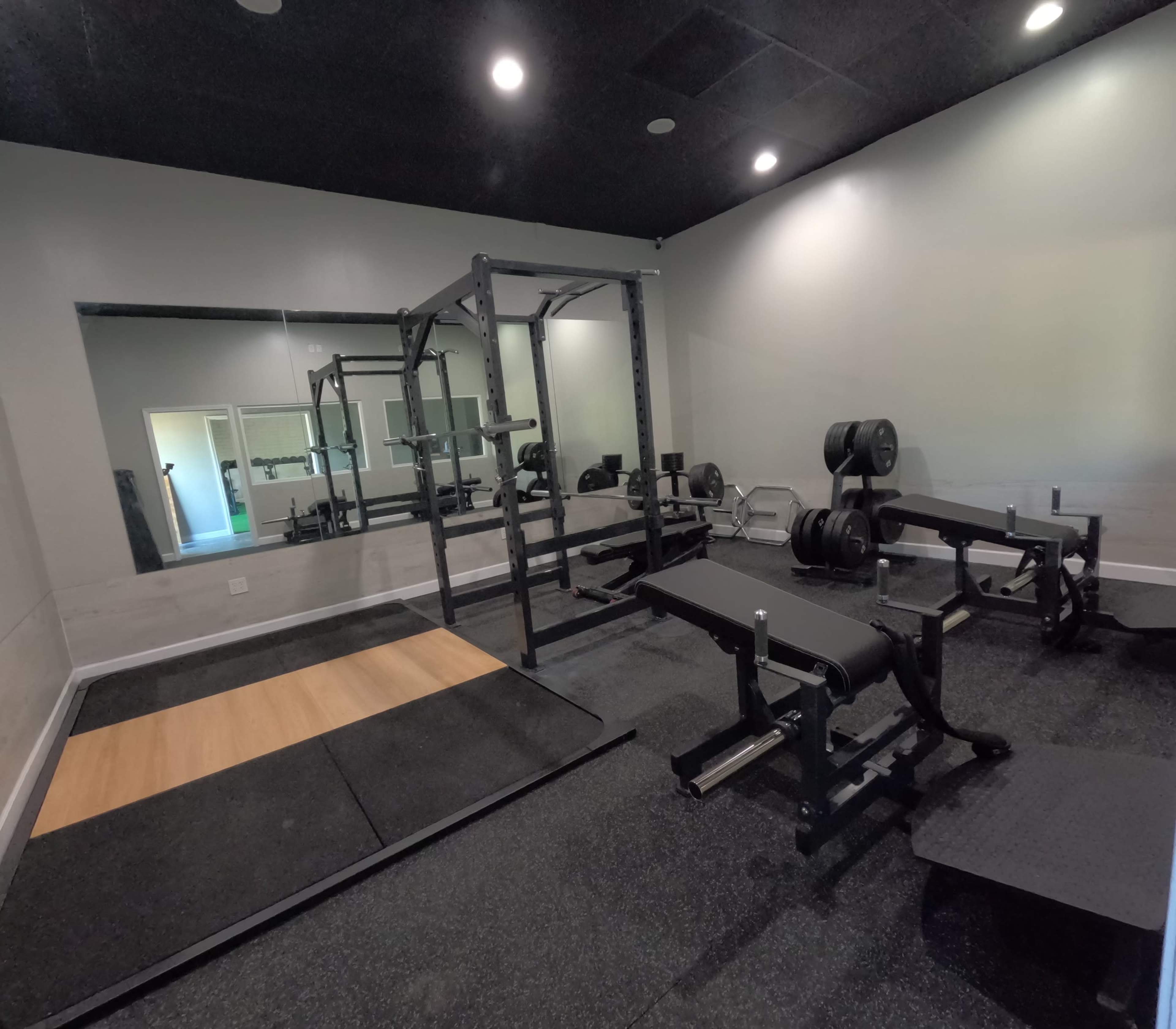 A gym interior featuring a power rack, weight plates, benches, and a mirrored wall.