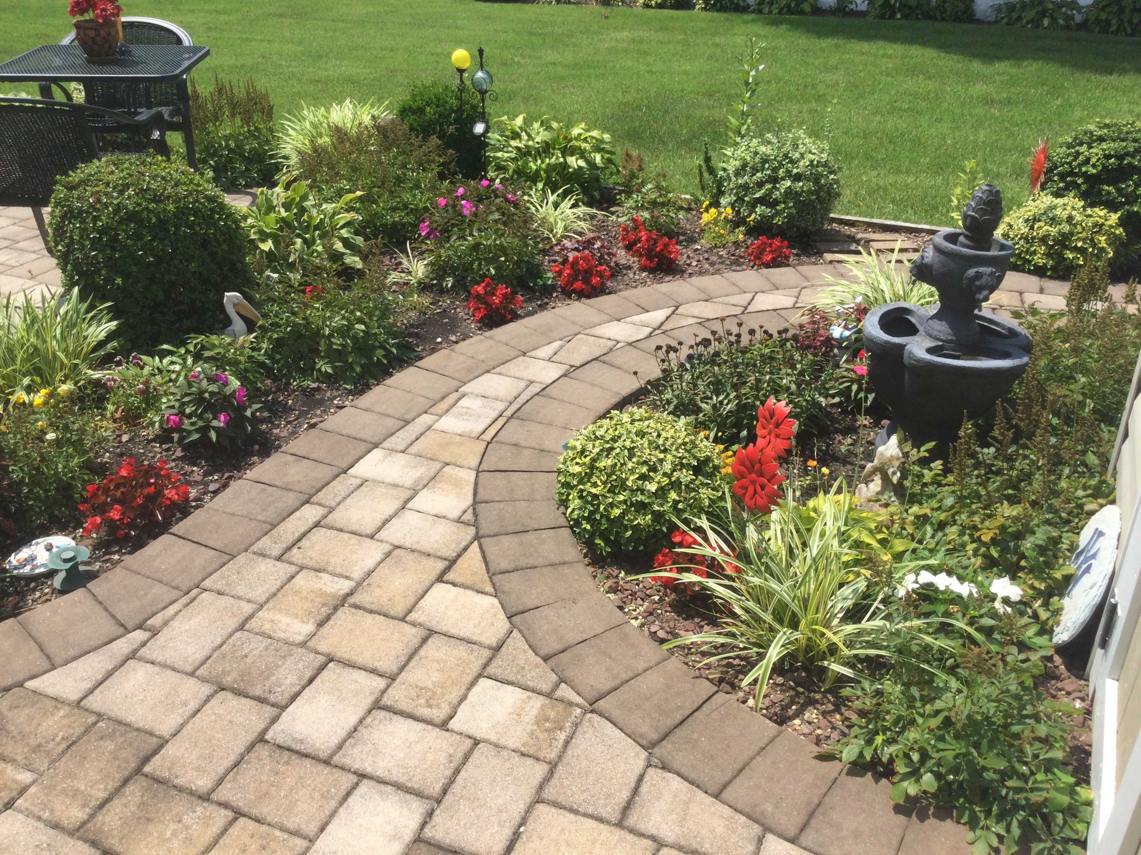A landscaped garden with a curved stone pathway, colorful flowers, and a small fountain surrounded by neatly trimmed bushes.