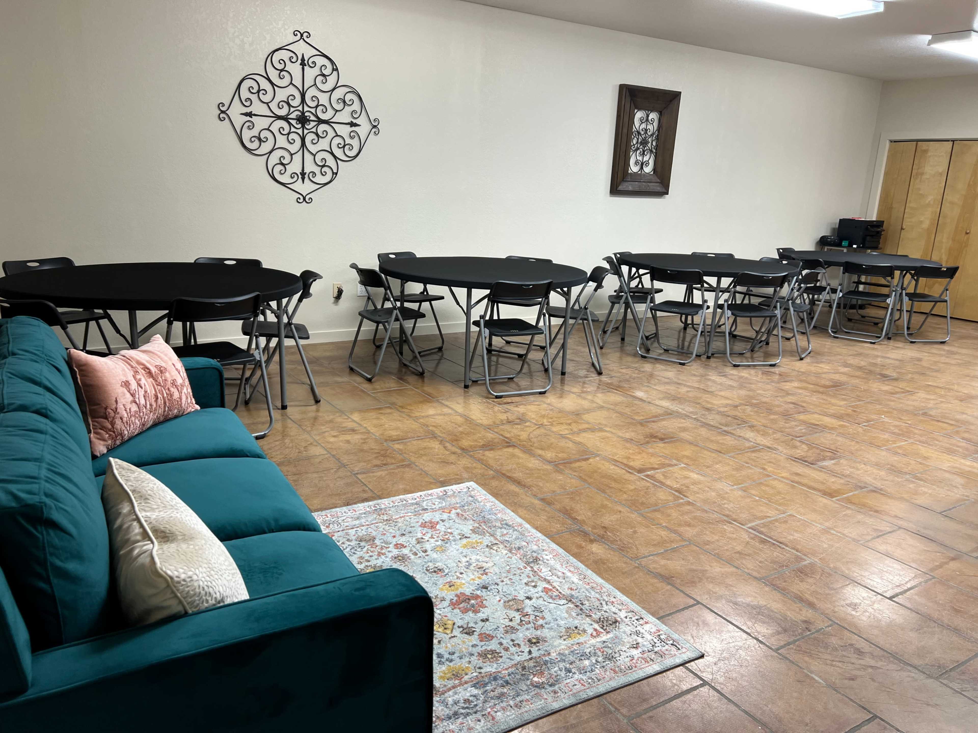 The room features a teal couch and several black folding tables arranged with chairs, along with decorative wall art.