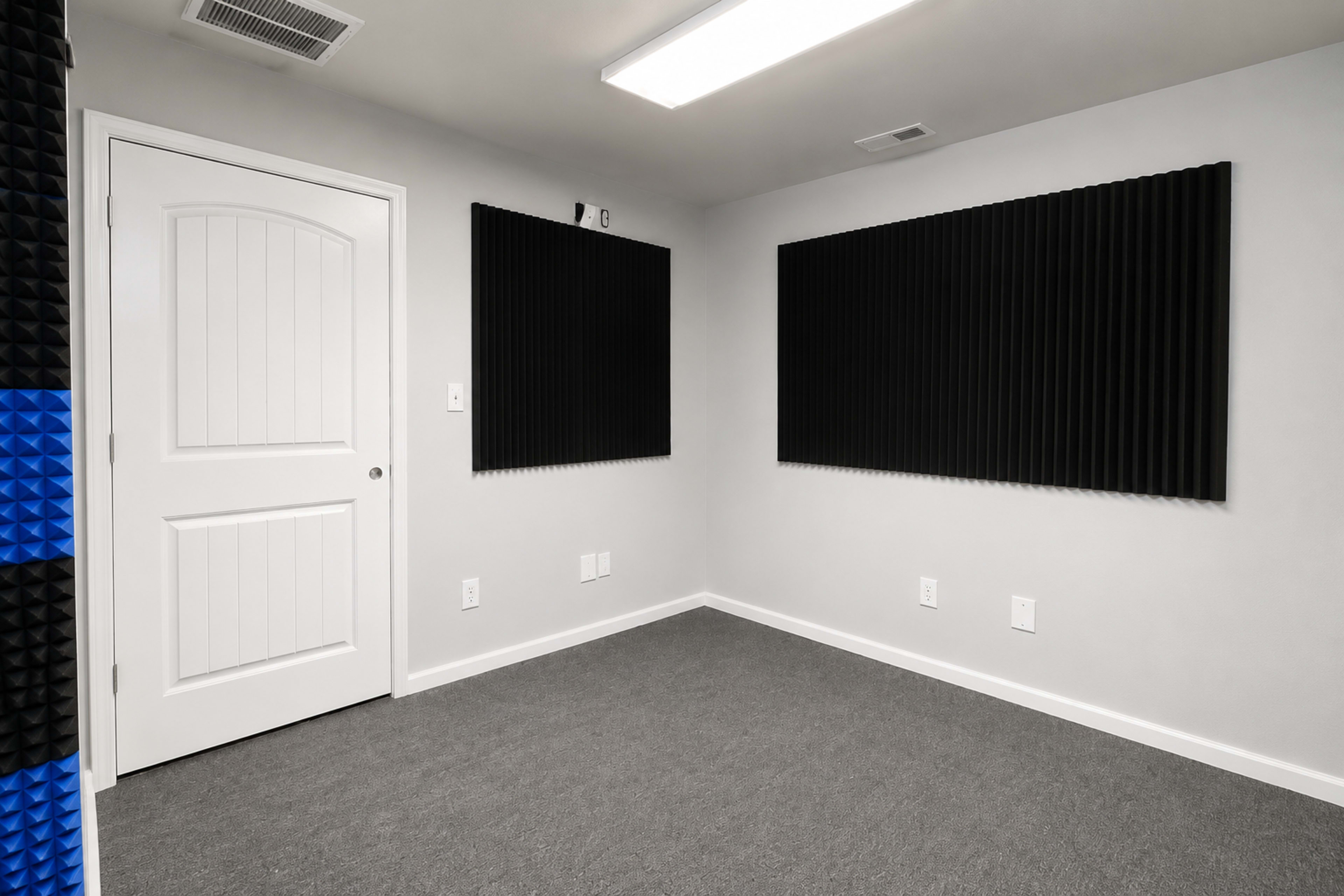 The image shows a soundproofed room with gray walls, a door, and two black acoustic panels mounted on the walls.