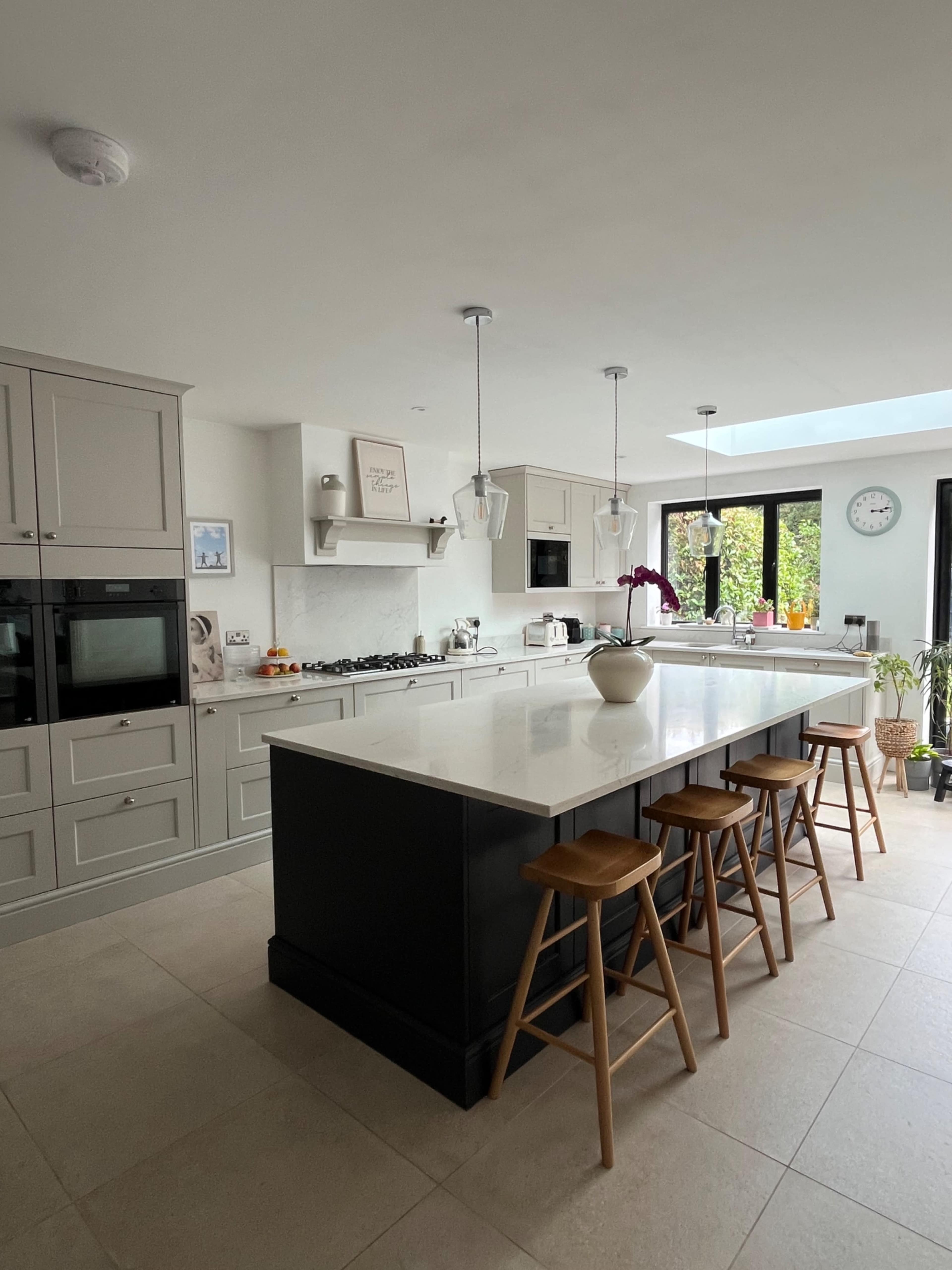 A modern kitchen features a central island with stools, sleek cabinetry, and large windows allowing natural light in.