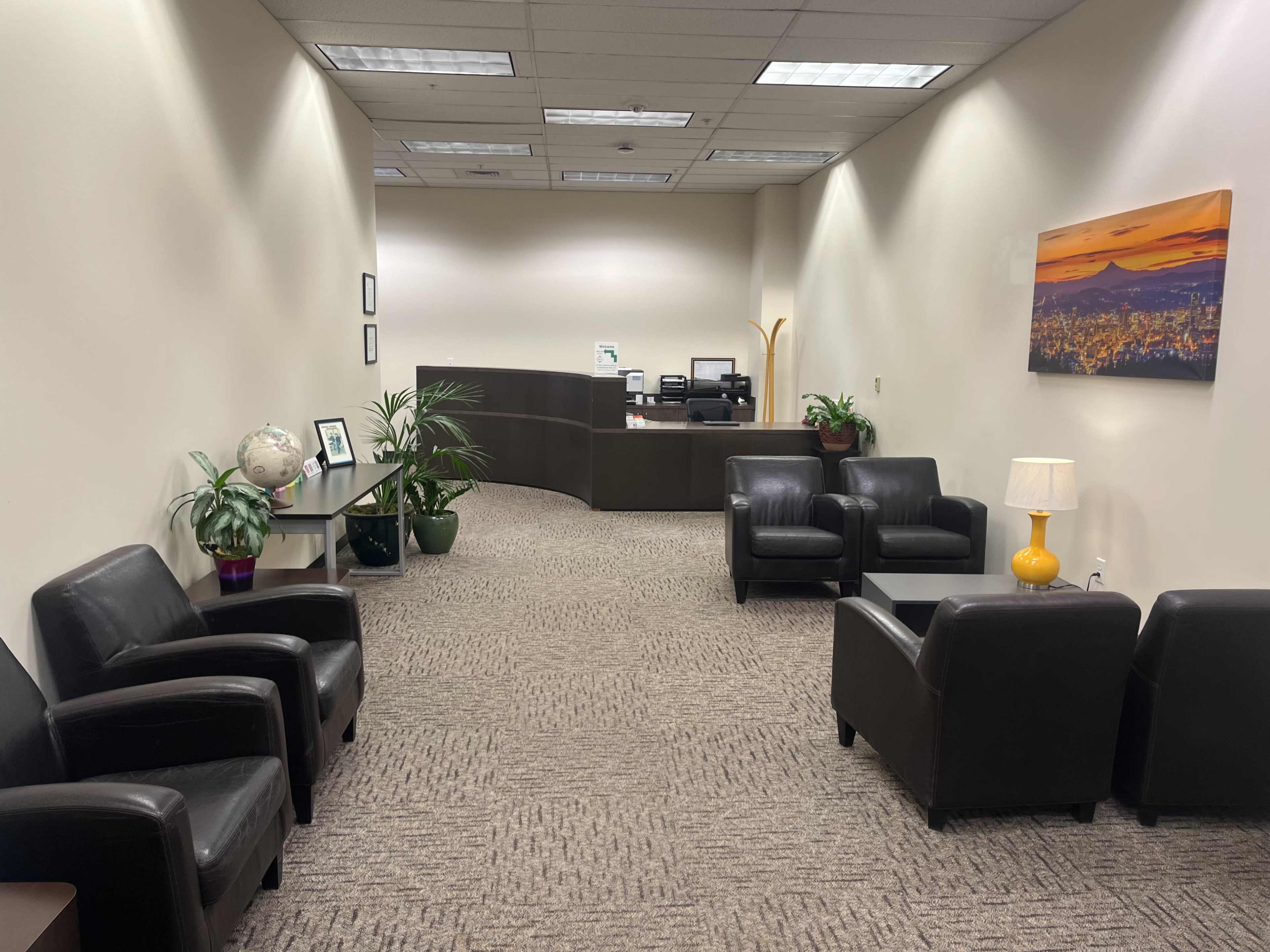 The image shows a reception area with two black armchairs and a small table, featuring a globe and plants, and a front desk in the background.