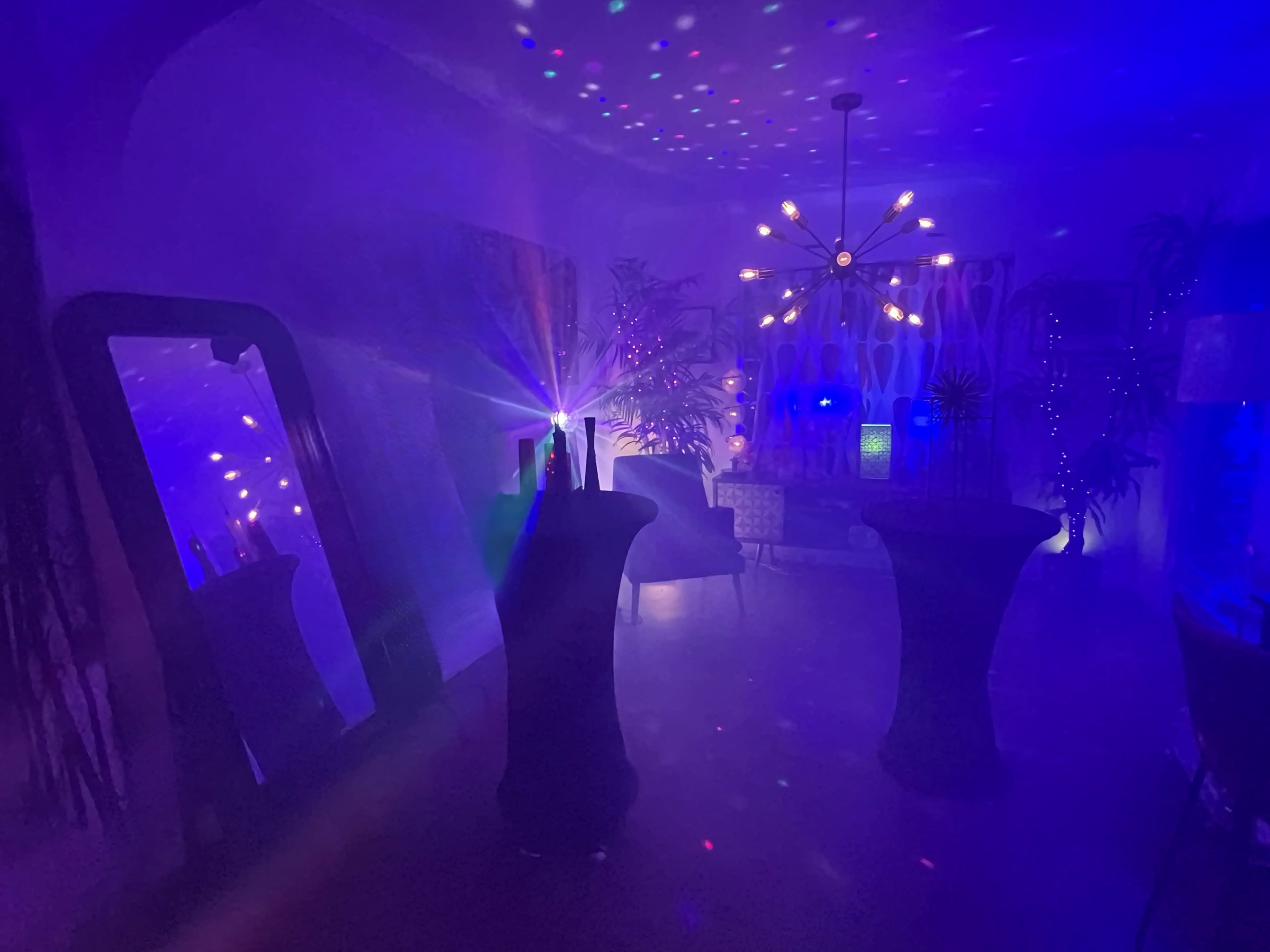 The image shows a dimly lit room with colorful lights creating patterns on the walls and a large mirror reflecting the ambiance.