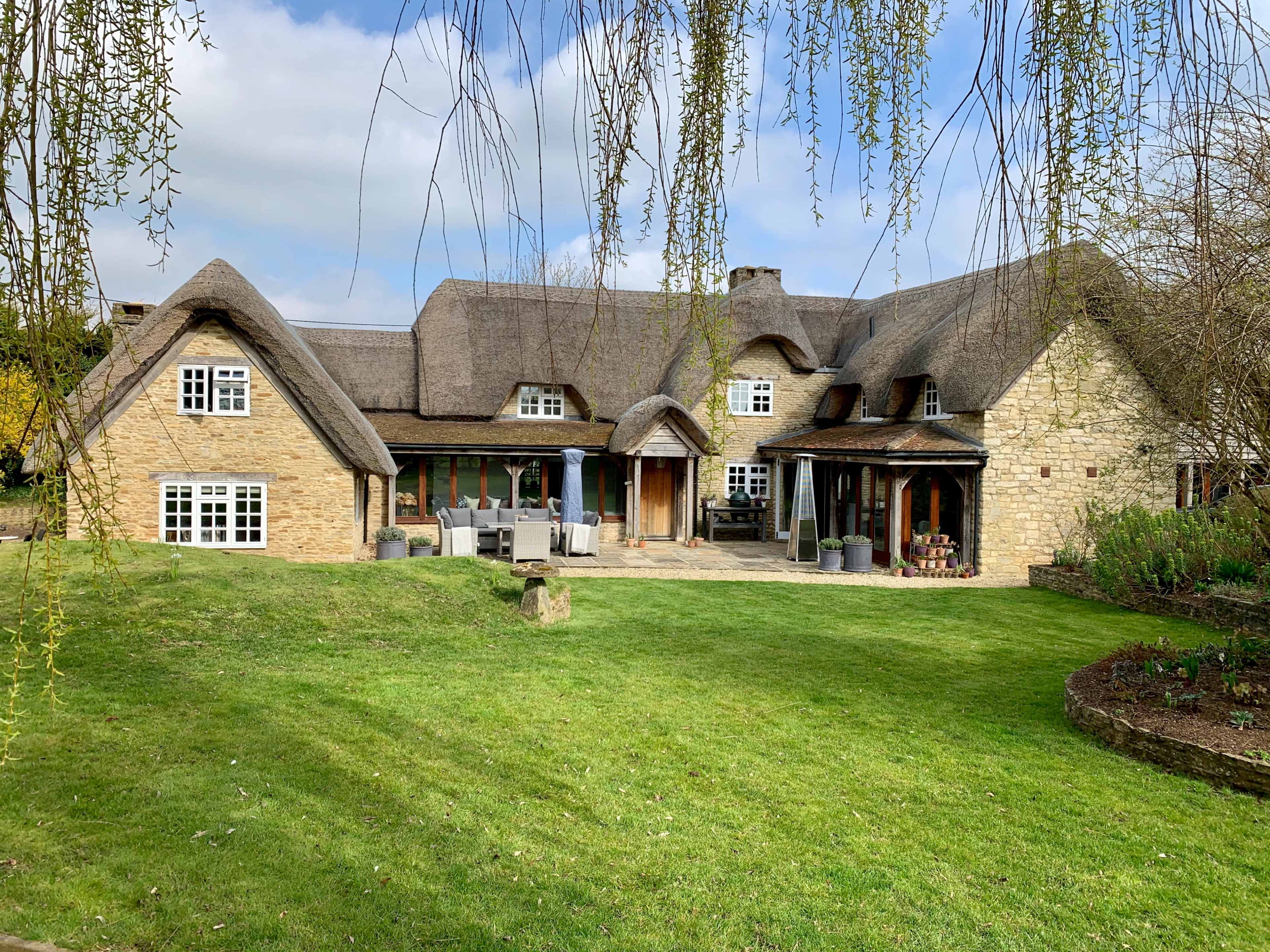 A spacious stone house with a thatched roof, surrounded by a well-maintained lawn and garden.