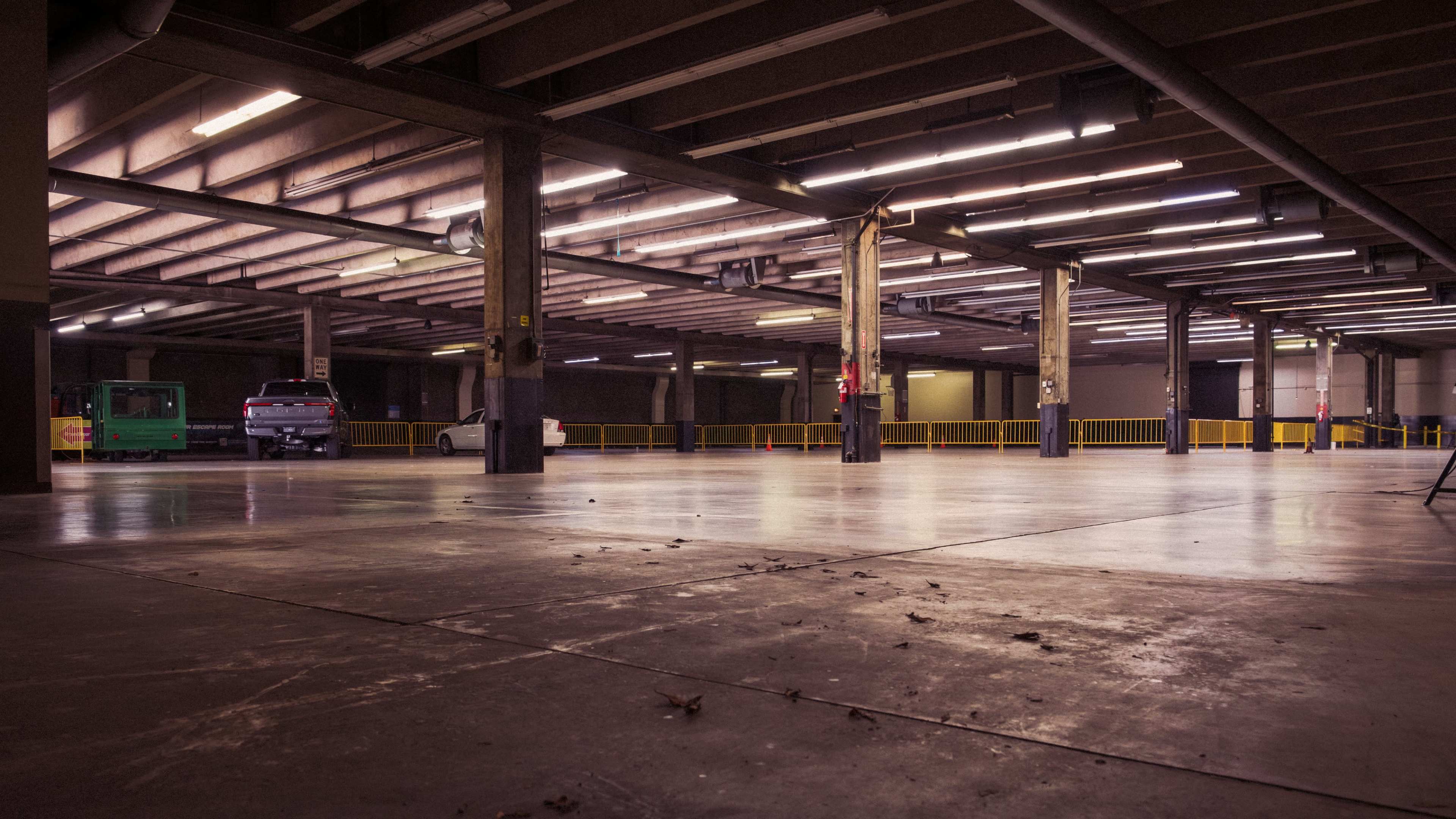 The image shows an empty parking garage with fluorescent lights and a few vehicles parked in the far corner.