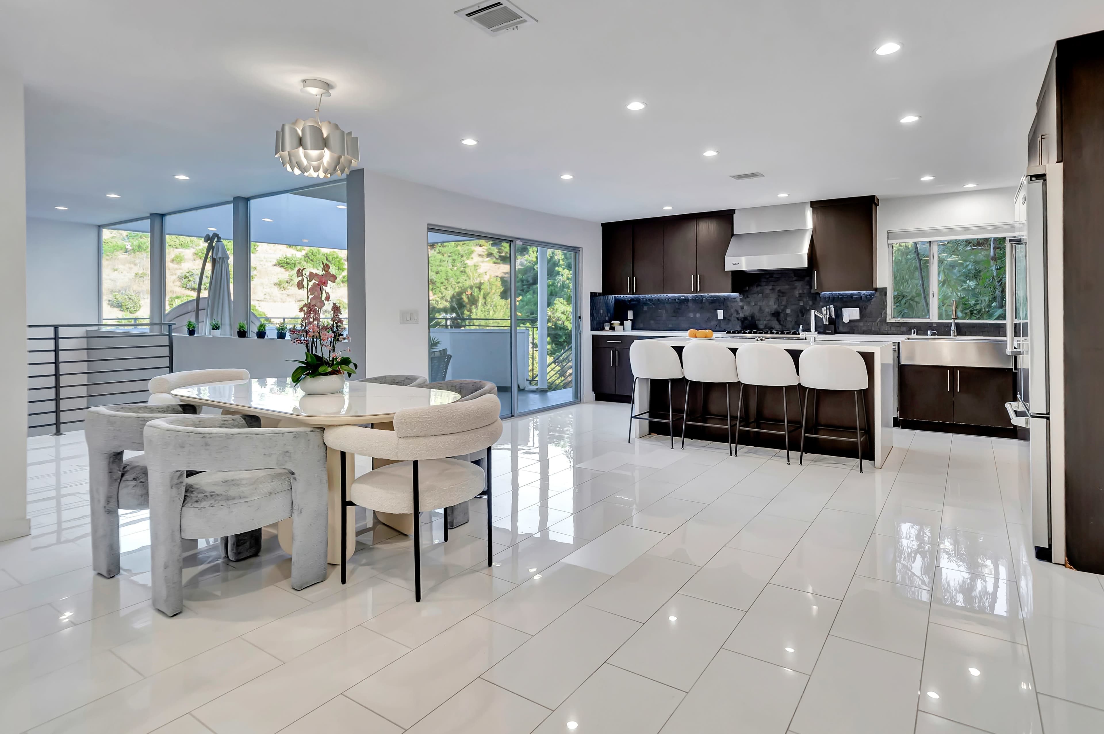 A modern kitchen and dining area featuring a circular table with chairs, a sleek kitchen island with bar stools, and large windows allowing natural light to illuminate the space.