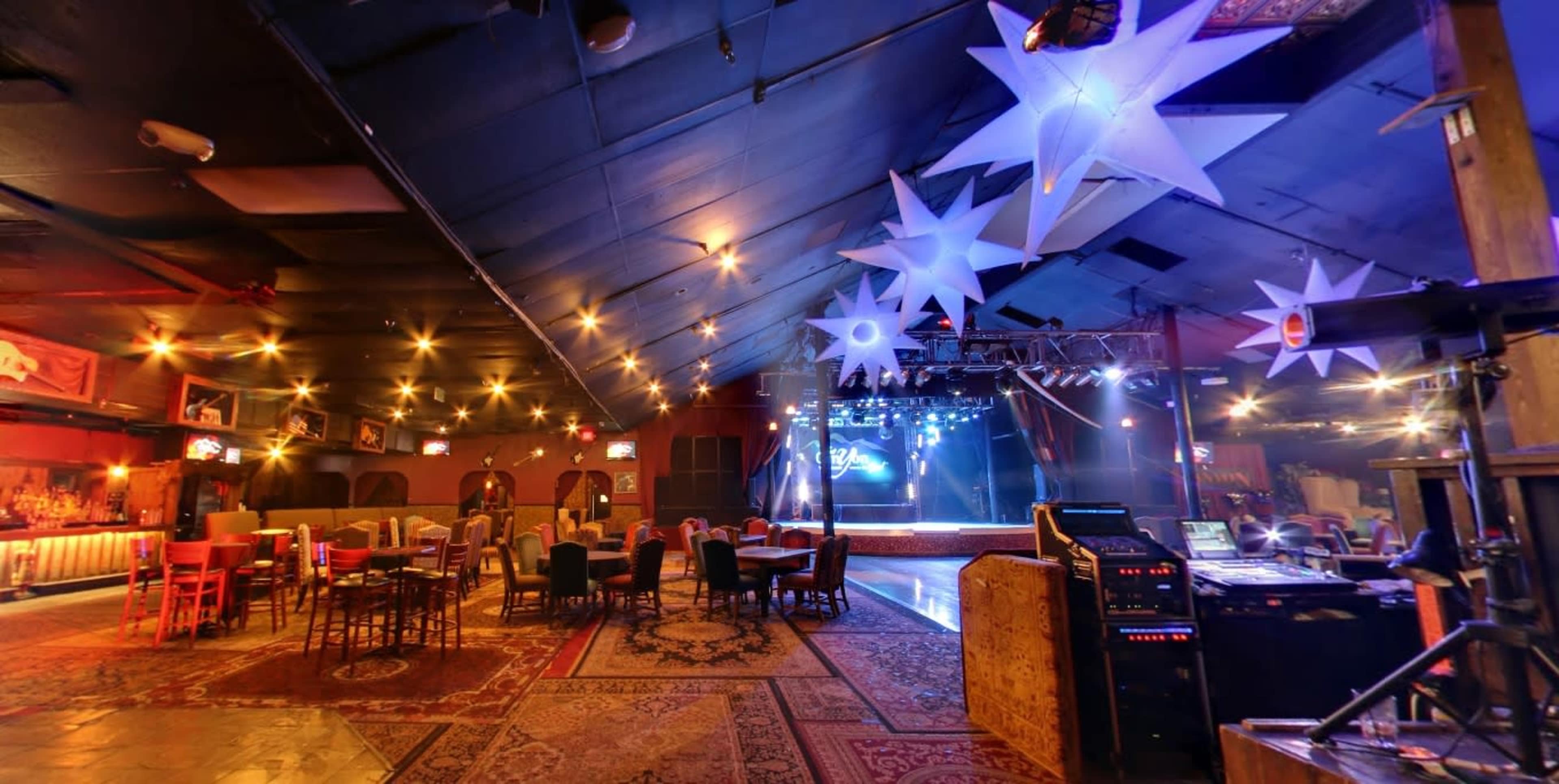 A spacious indoor venue with a stage at the front, decorated with star-shaped lights and surrounded by tables and chairs.