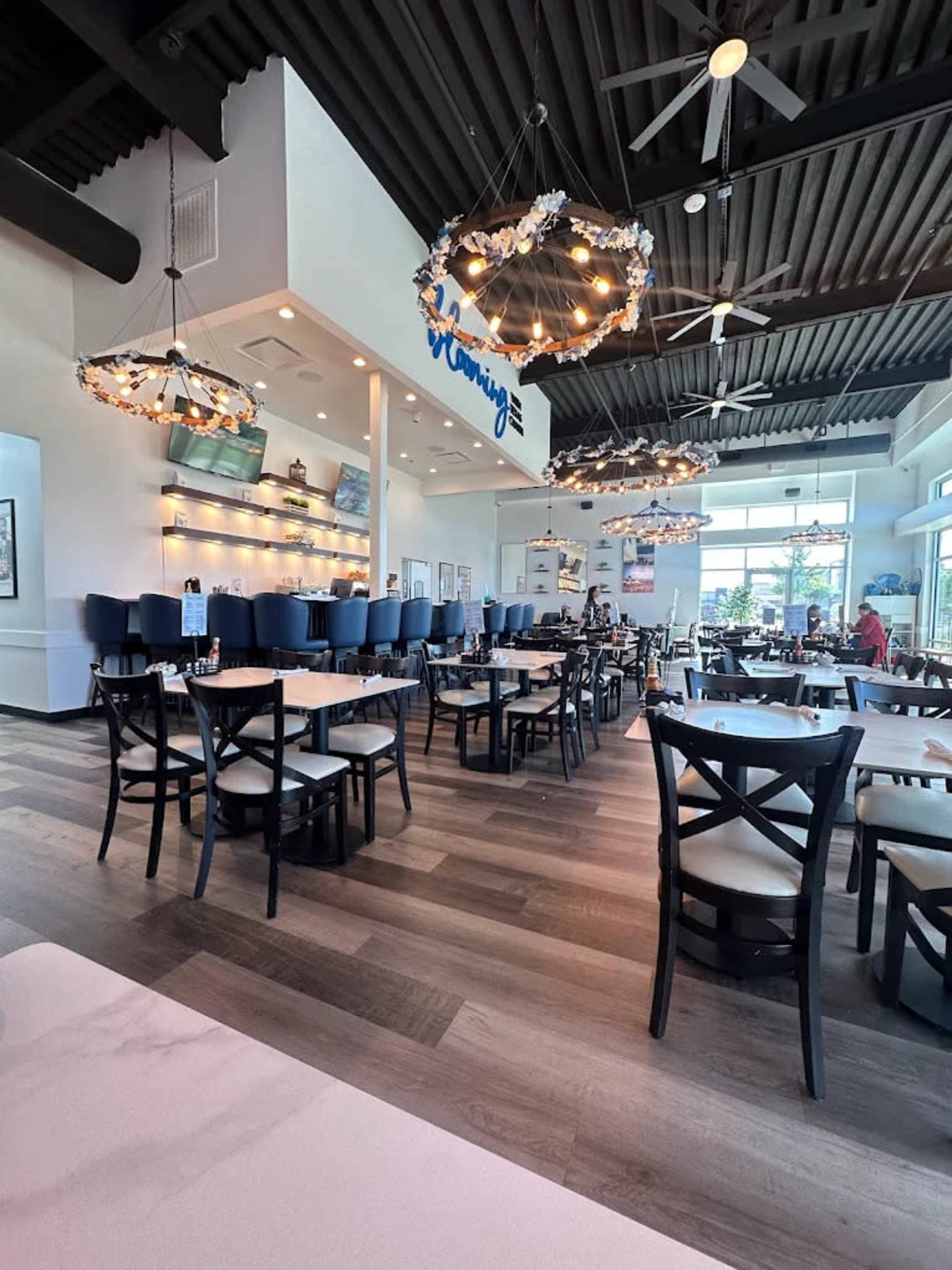 The image shows a spacious restaurant with wooden flooring, blue seating, and modern light fixtures hanging from the ceiling.